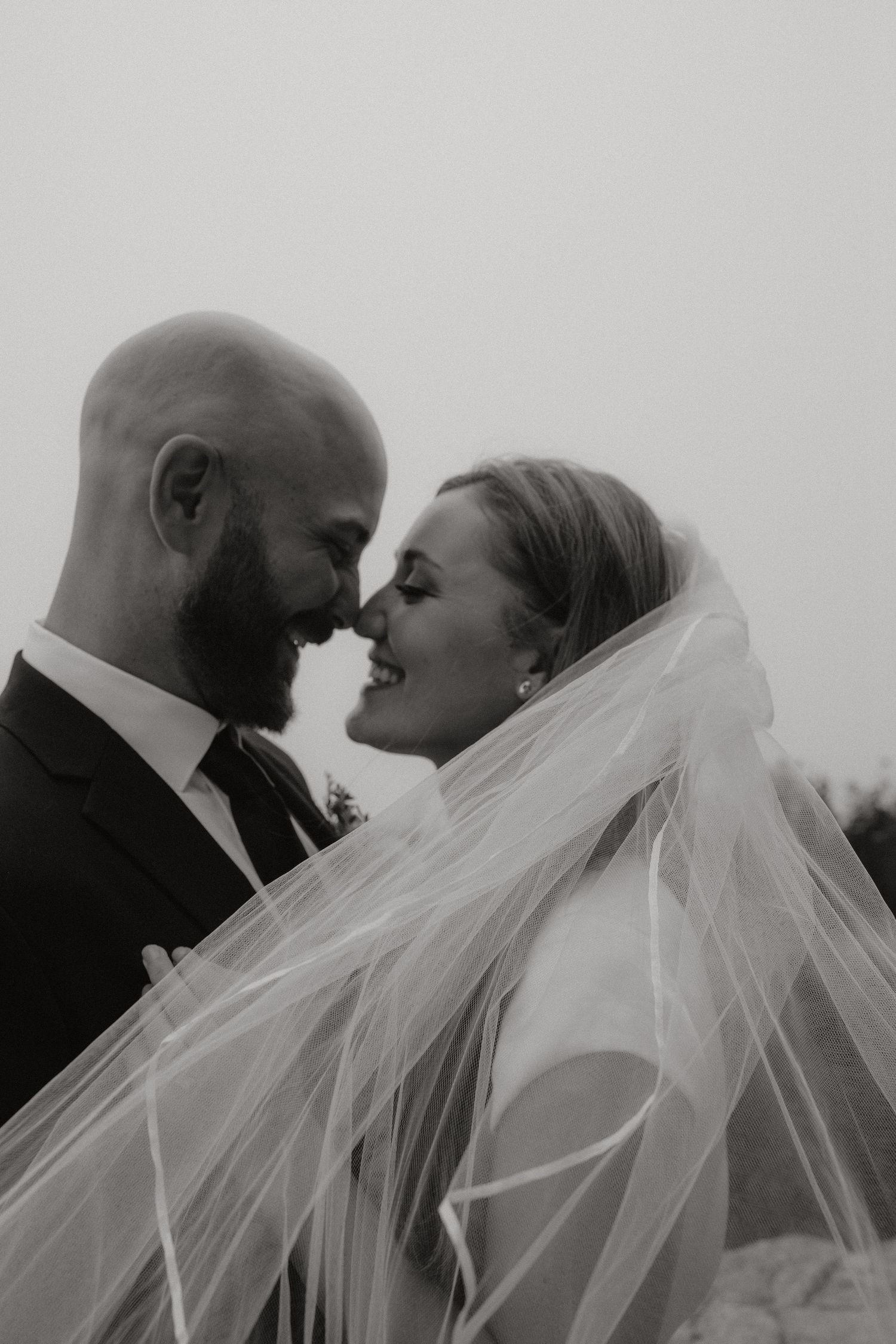 Intimate black and white portrait of newlyweds with flowing bridal veil.