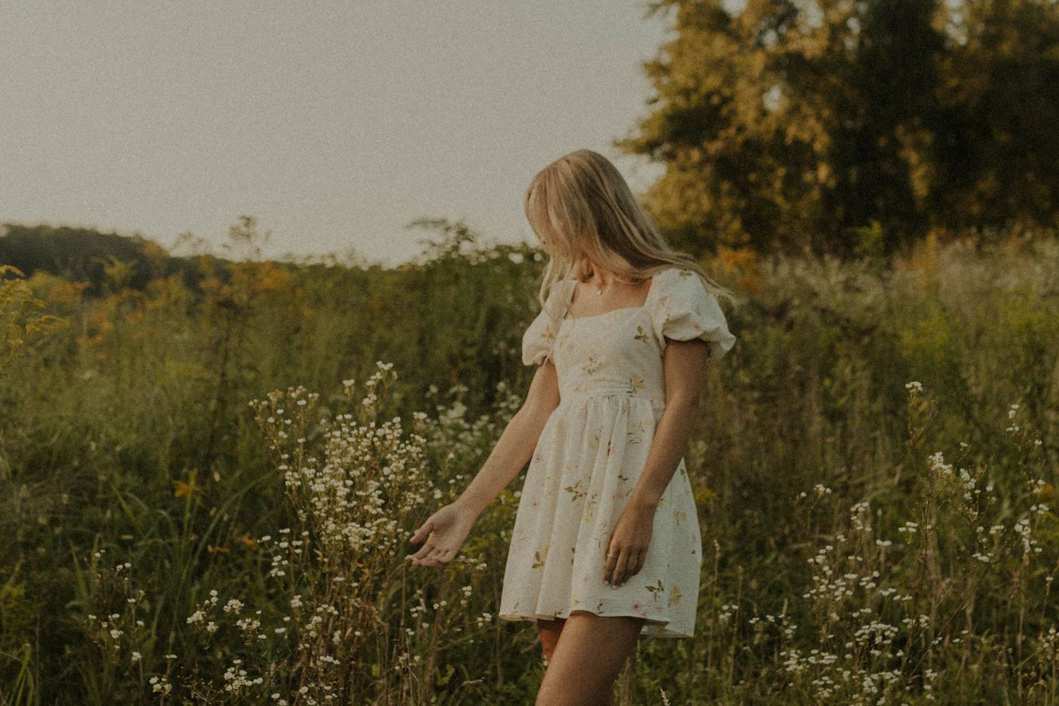 Person in white summer dress walks through wildflower meadow at golden hour.