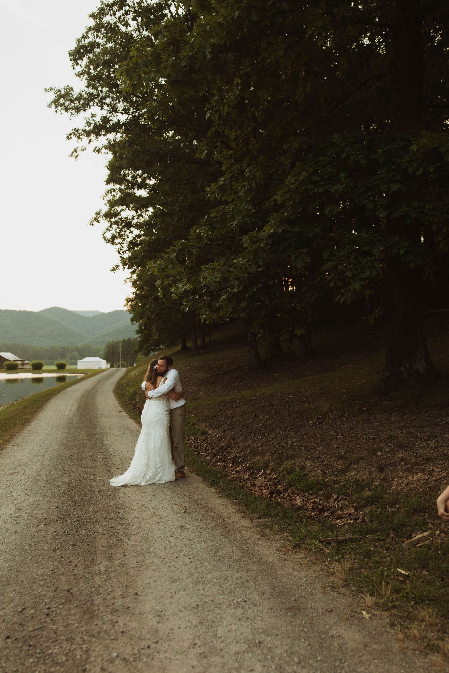 A couple embraces on a country road with mountains and trees in the background.