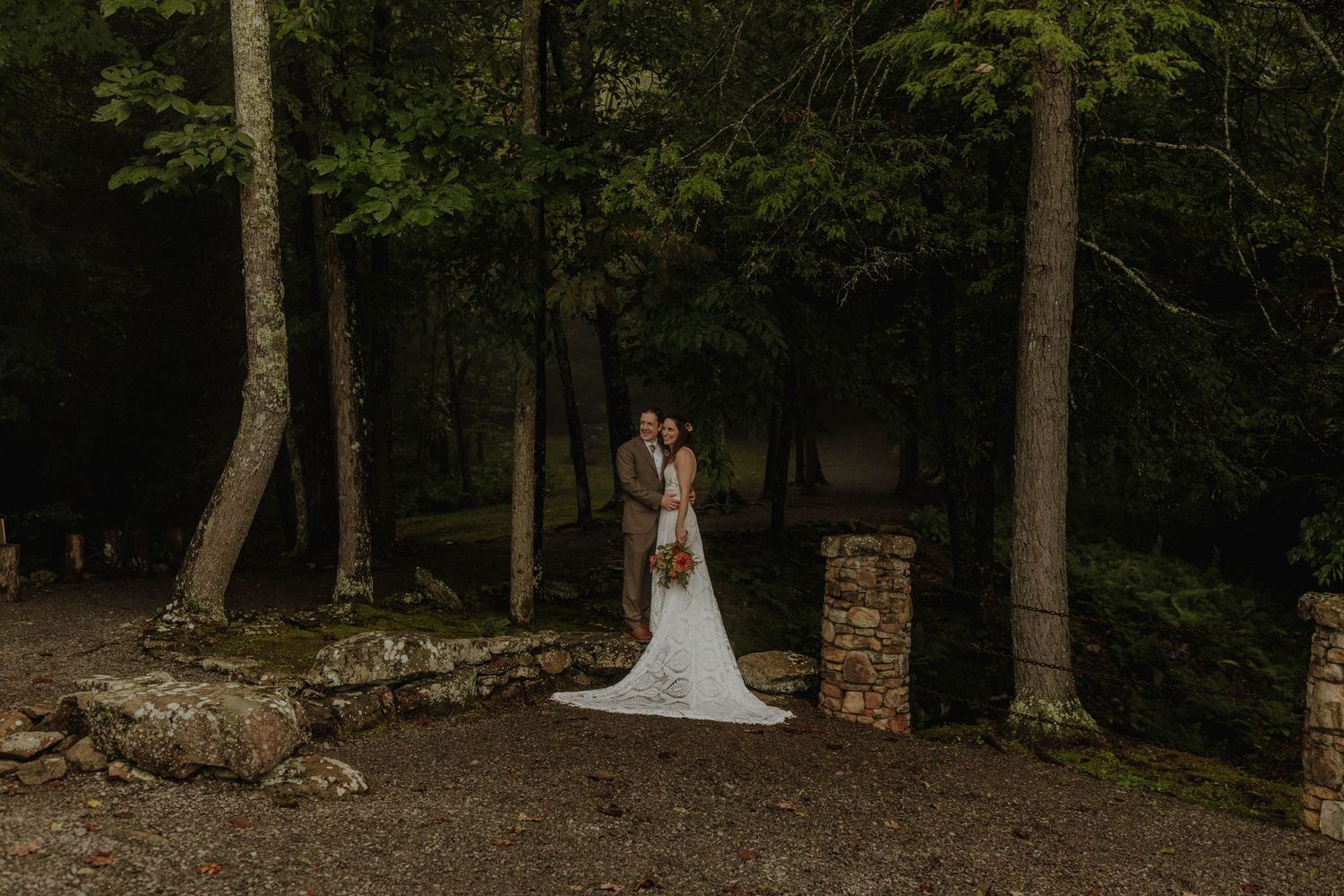 A romantic wedding moment captured between stone pillars in a serene forest setting.