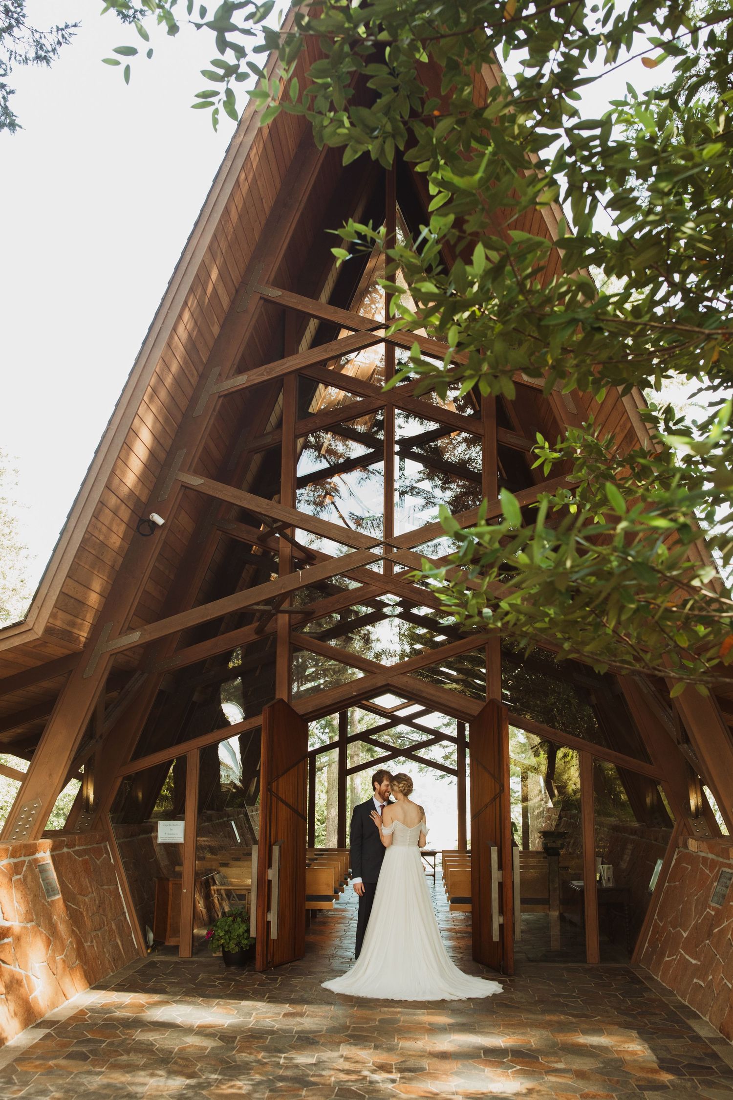 A couple poses under a dramatic wooden chapel structure with soaring architectural beams.
