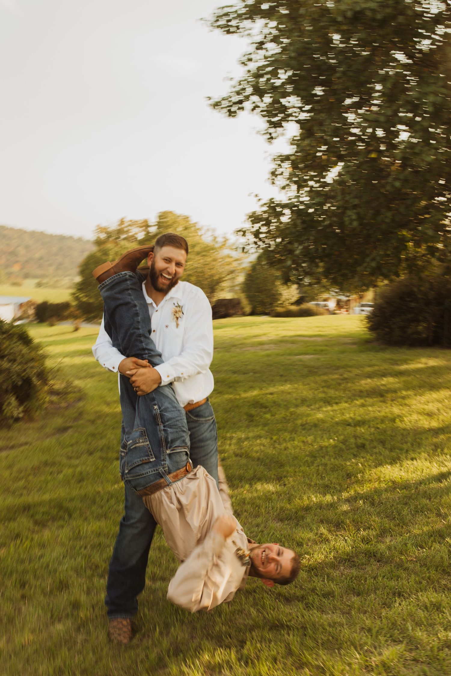 A playful moment captured outdoors with someone being held upside down on a grassy hill.