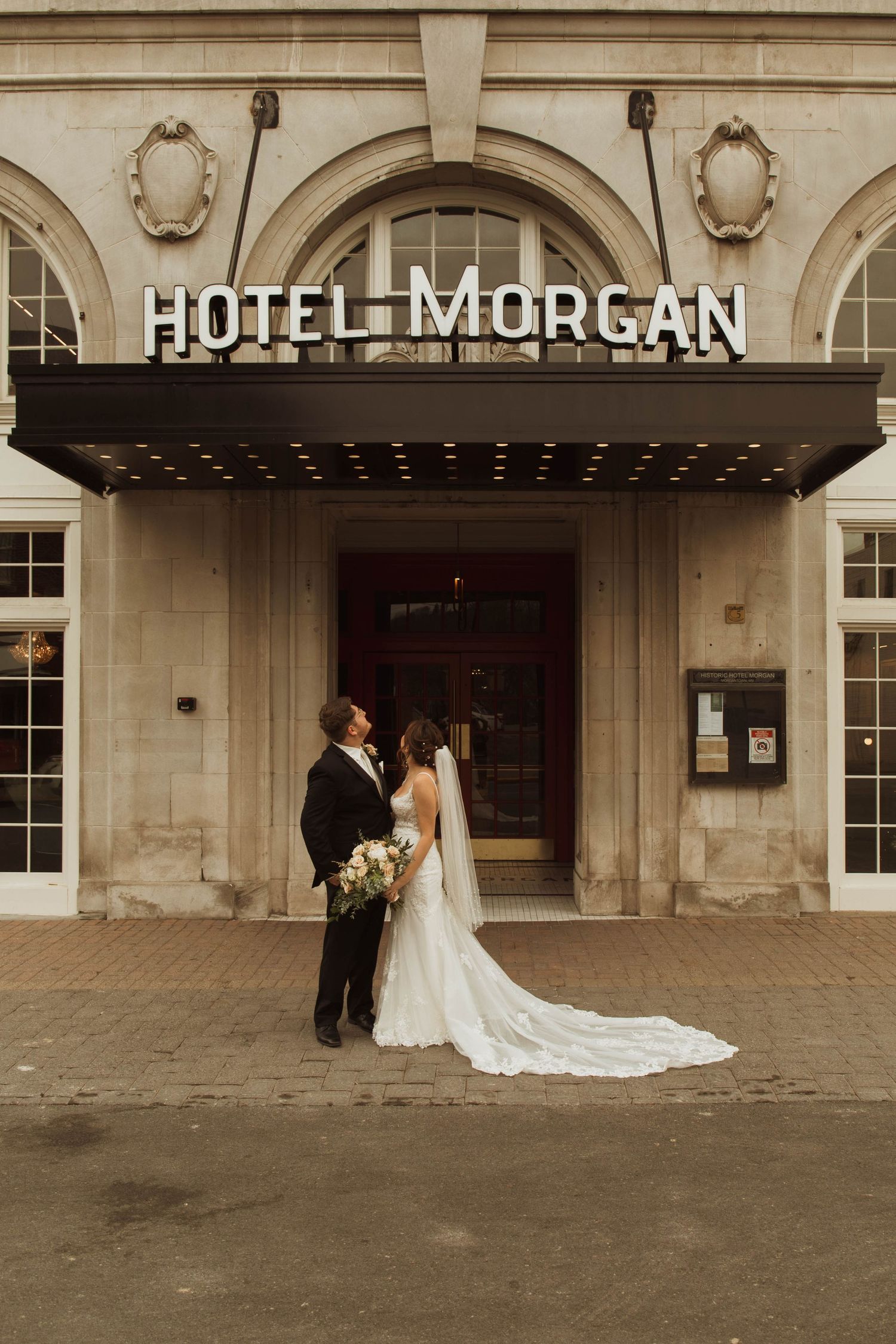 A wedding couple poses beneath the classic Hotel Morgan entrance sign and archway.