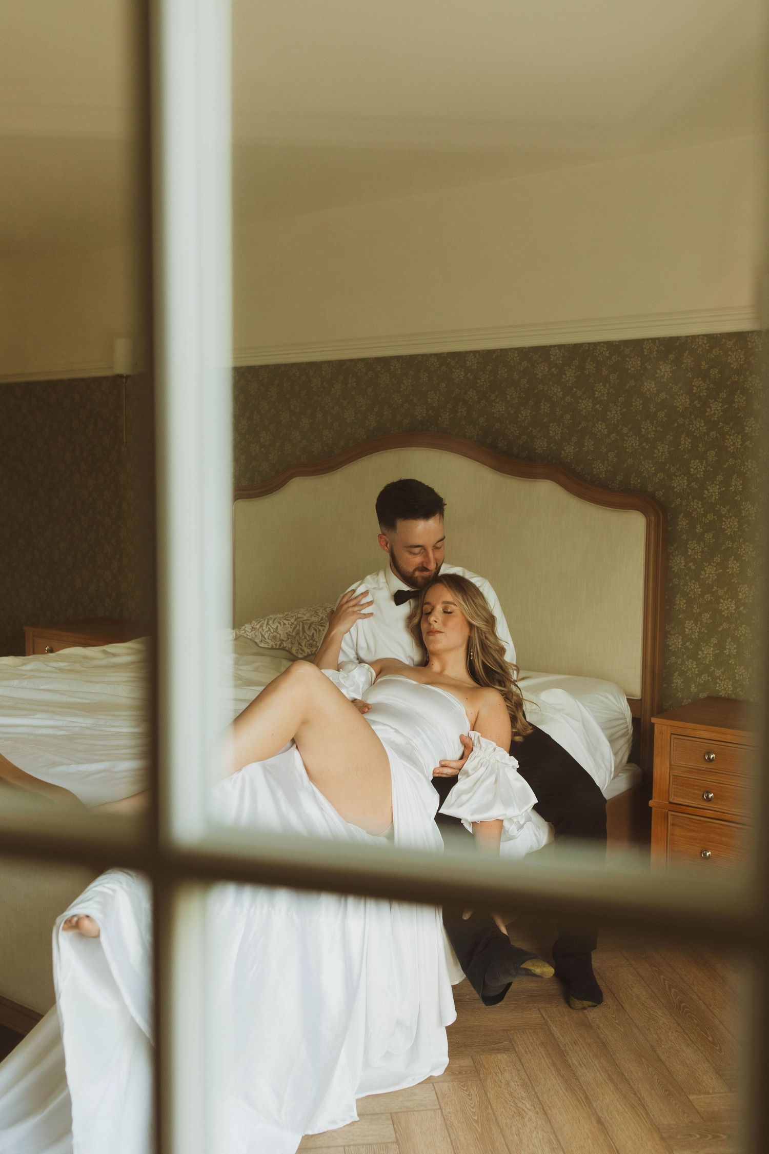 An intimate wedding portrait captured through window panes in warm lighting.