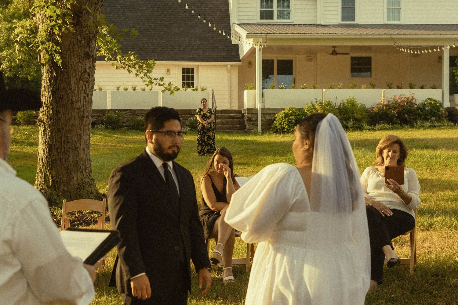 Golden hour backyard wedding ceremony with string lights and rustic farmhouse backdrop.