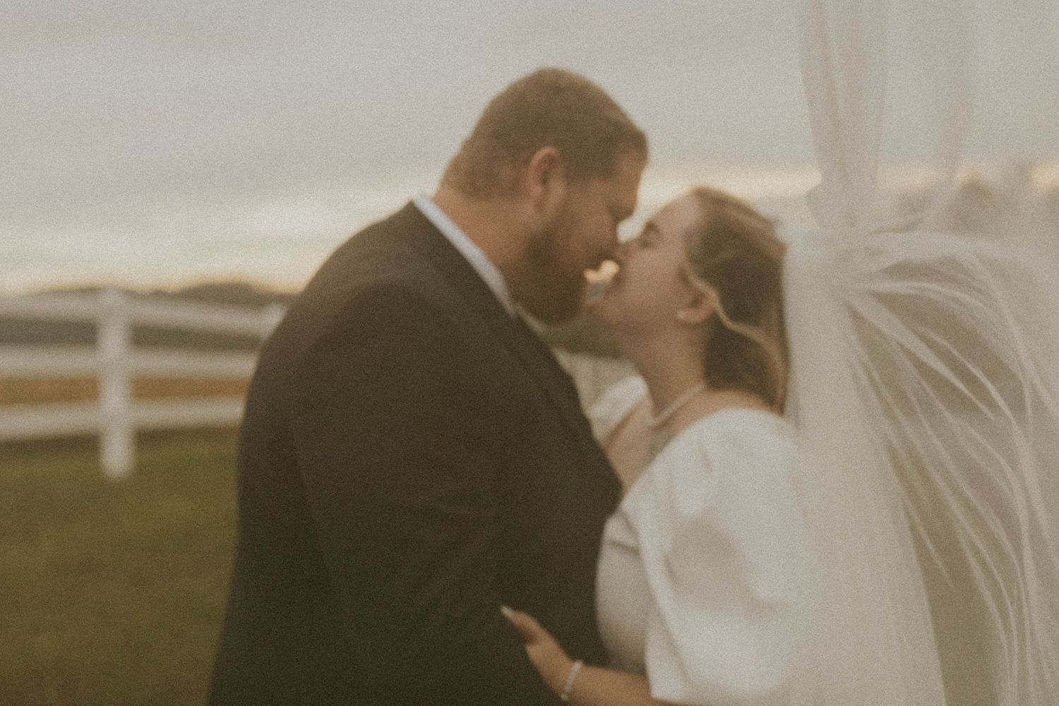 Romantic vintage-style wedding portrait in muted tones by white fence.