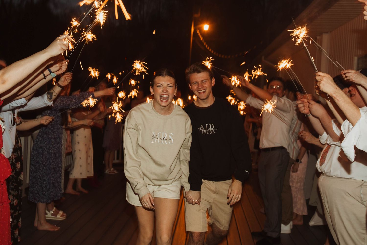 Wedding couple walking through sparkler exit tunnel at nighttime celebration.