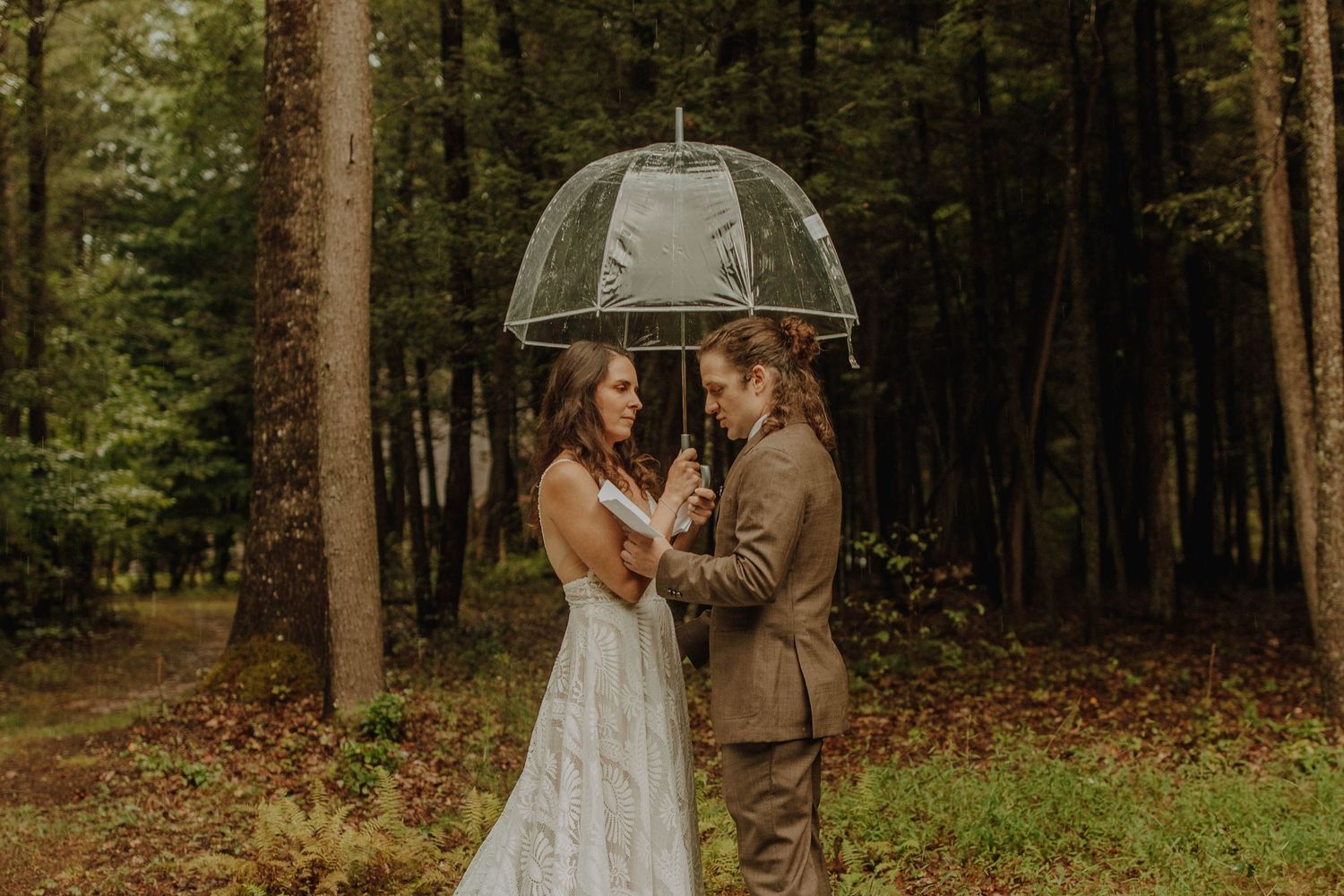 An intimate forest wedding portrait with a clear umbrella and autumn colors.