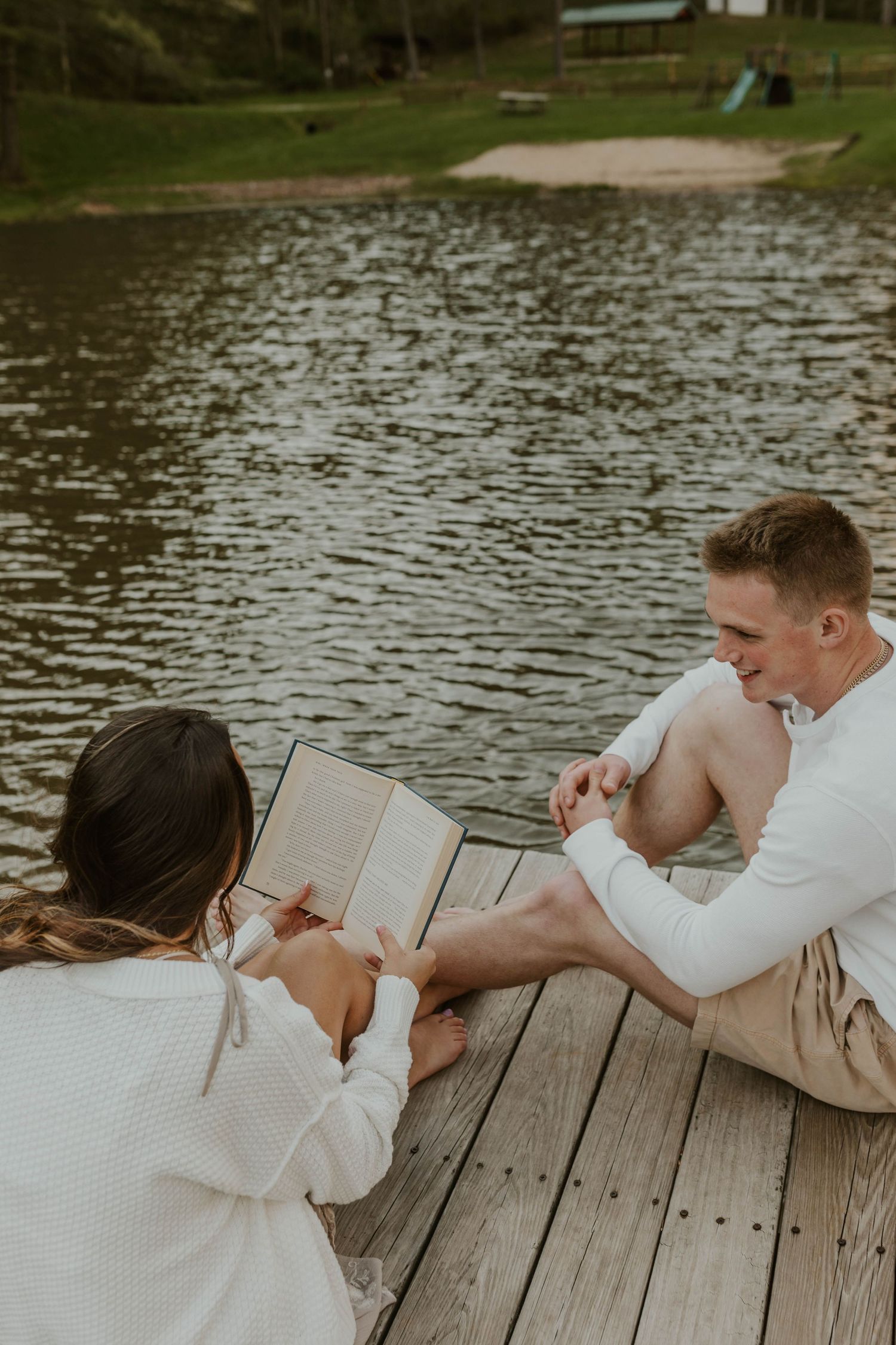 Reading together on wooden dock by the lake in warm sweaters.