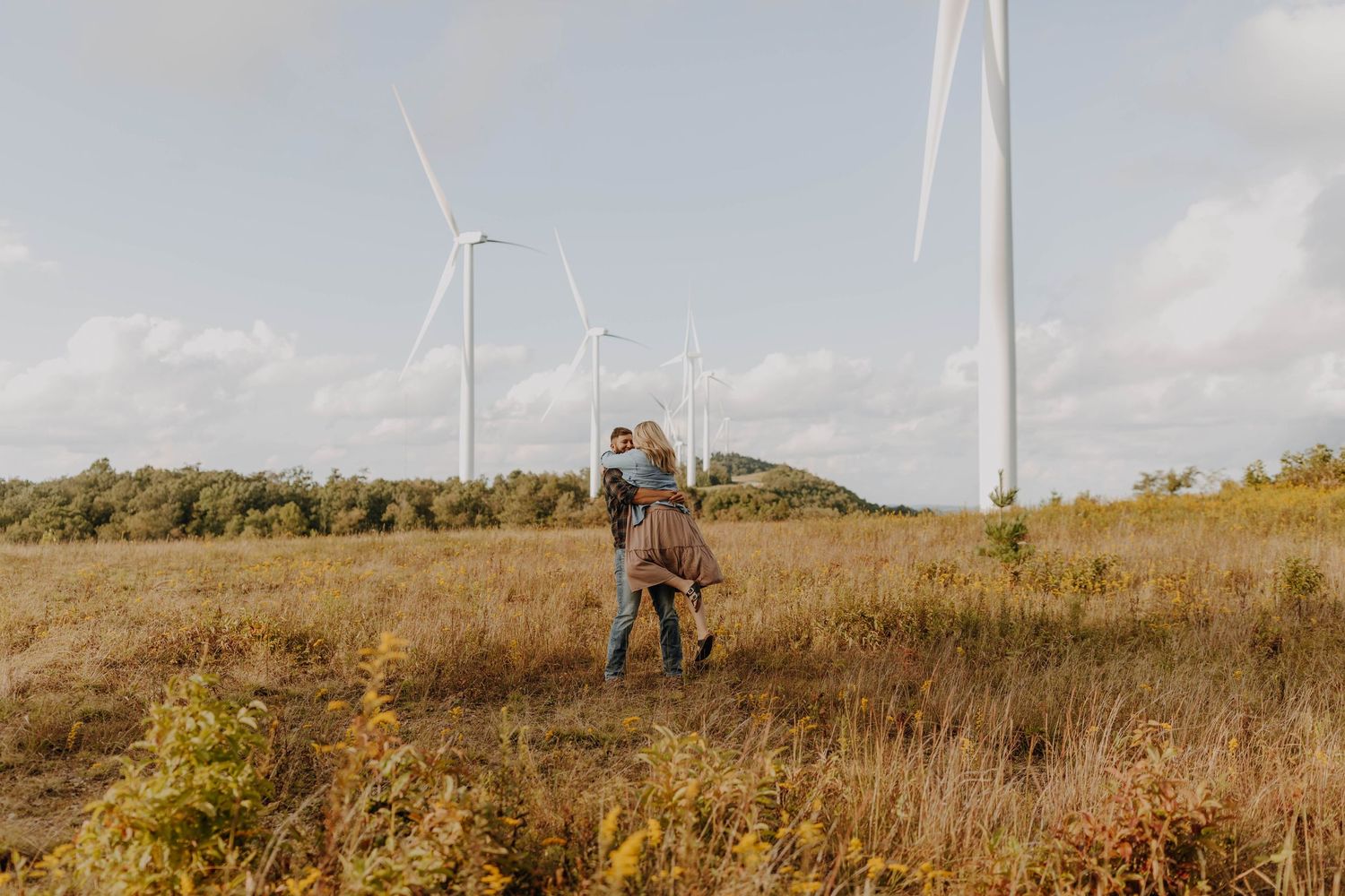 Person standing in field with wind turbines in background during daytime.
