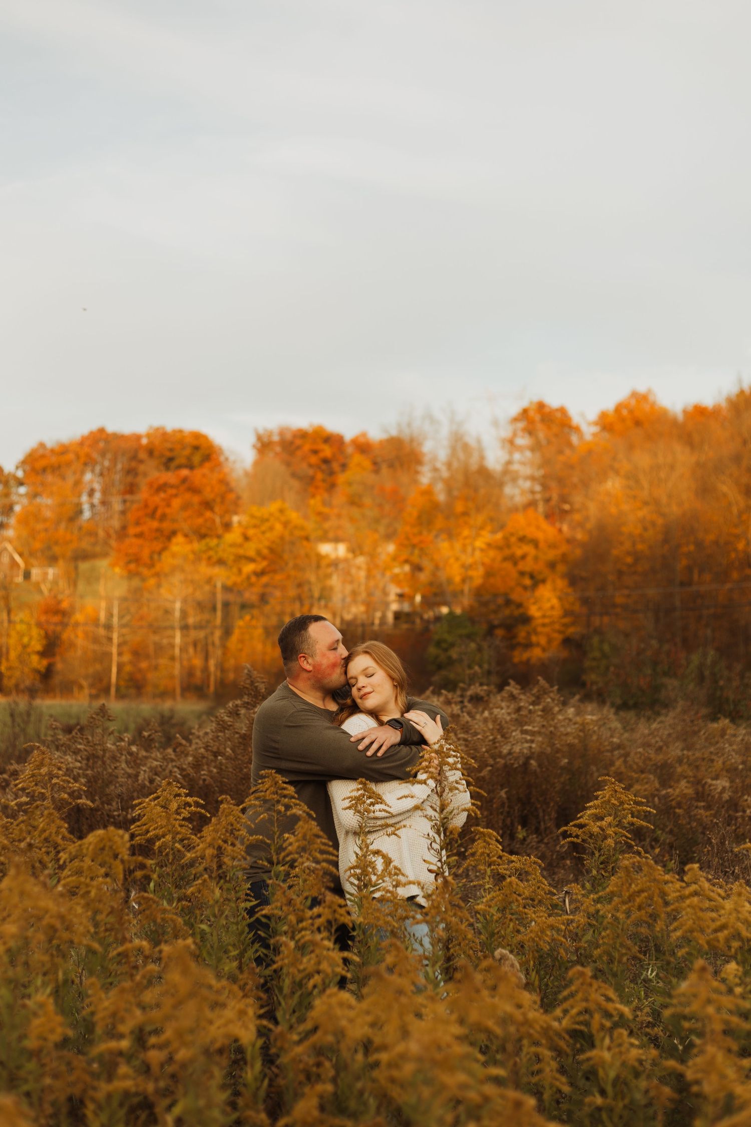 A romantic embrace in a field of golden autumn foliage with fall trees in the background.