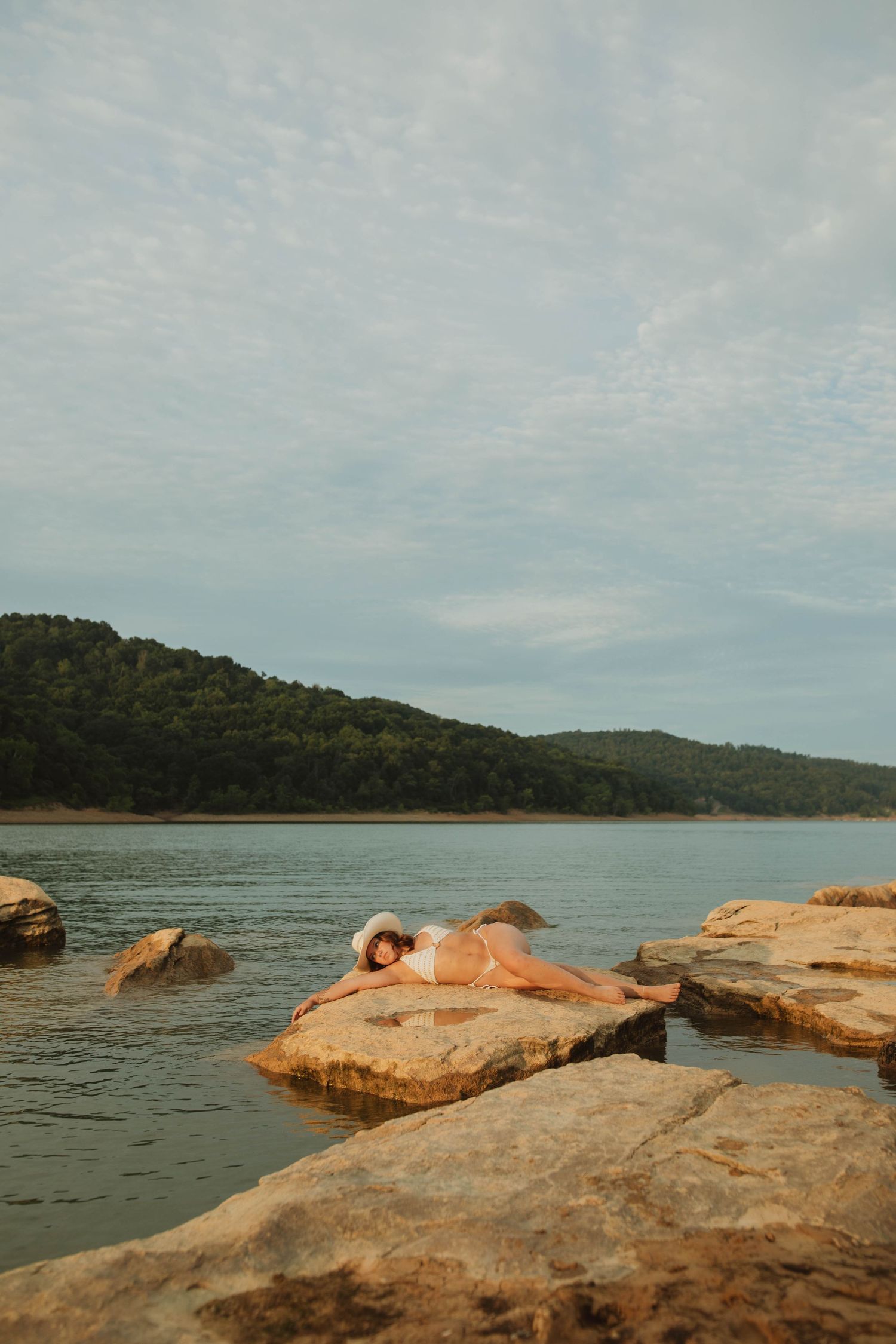 Scenic lakeside landscape with rocky formations and distant tree-covered hills.