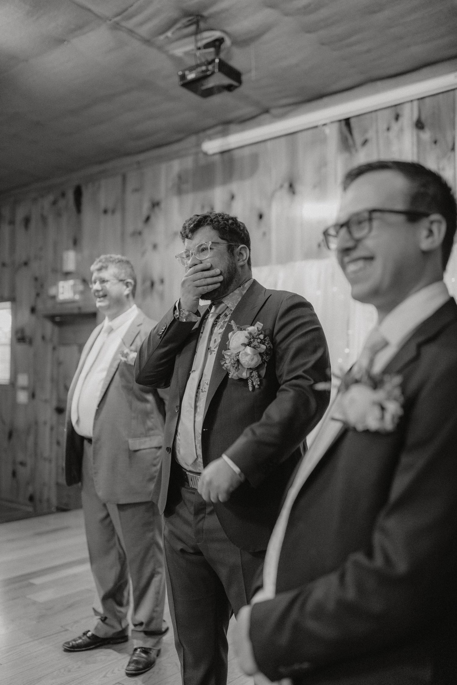 Black and white photo of groomsmen having an emotional reaction during wedding ceremony.