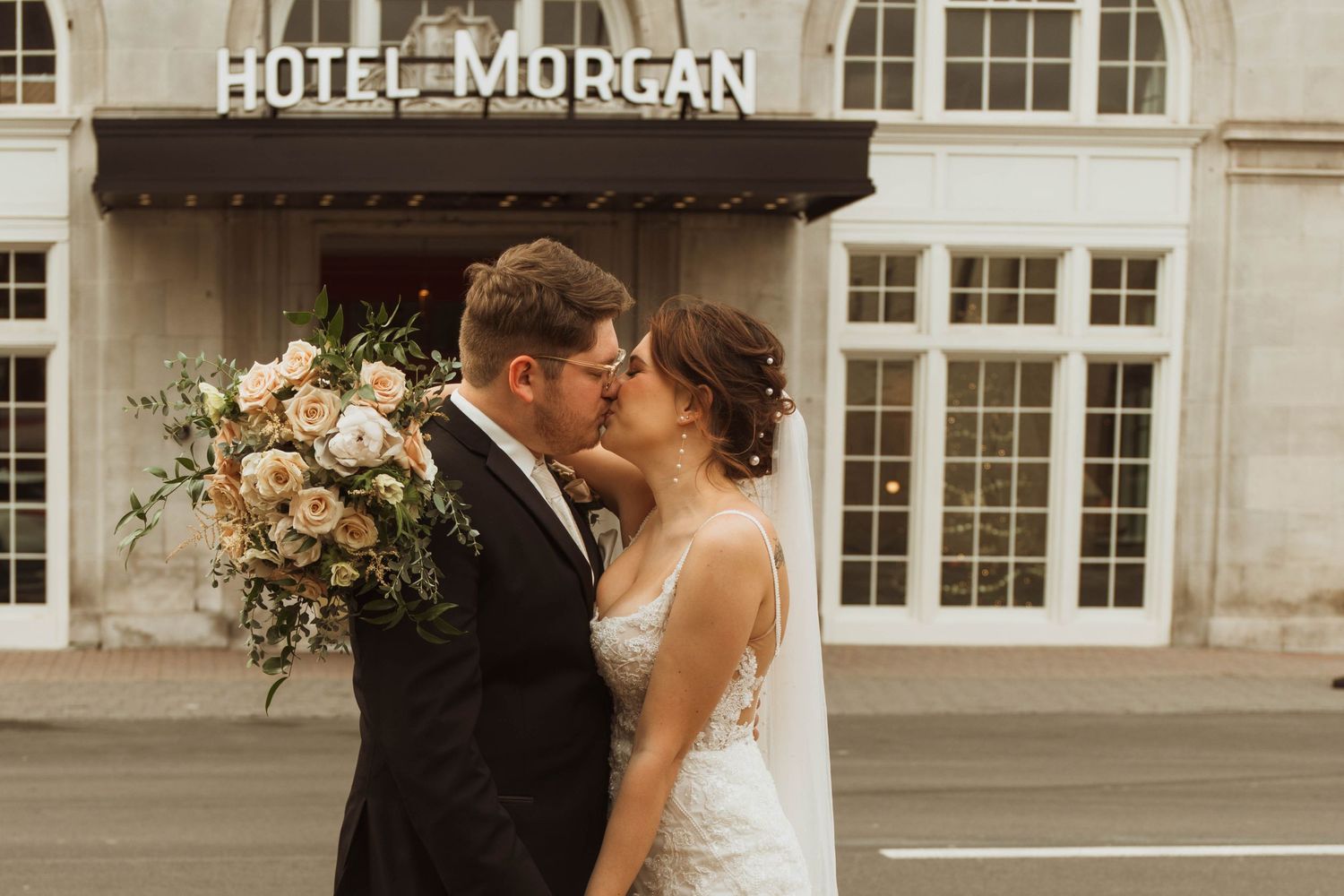 A romantic kiss shared by newlyweds outside the historic Hotel Morgan entrance.