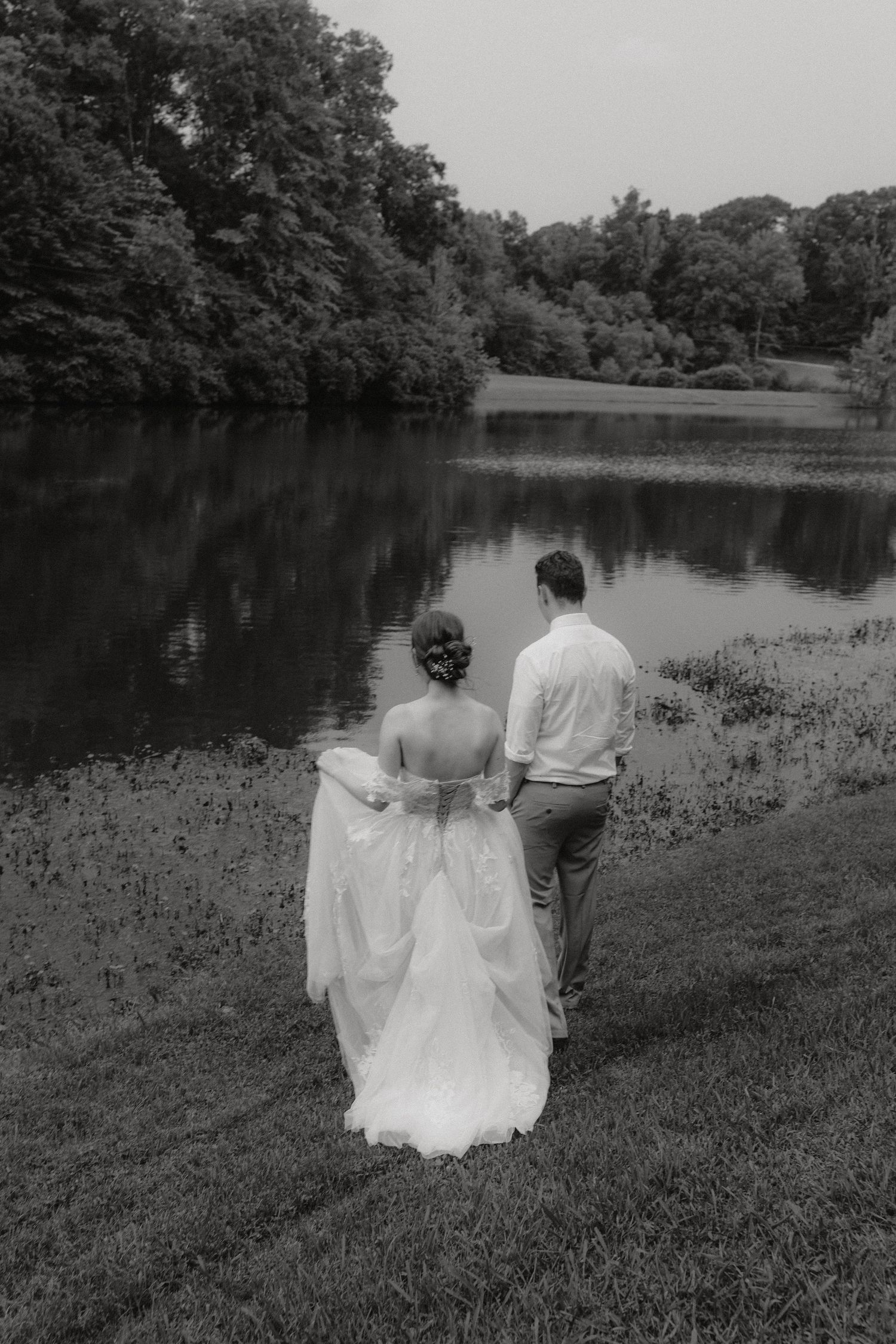 Black and white photograph of couple overlooking peaceful lake landscape.