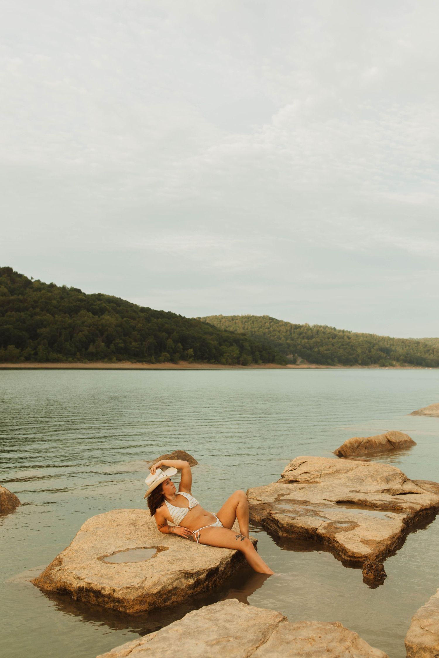 Artistic photo of someone reclining on lakeside rocks during a peaceful sunset.