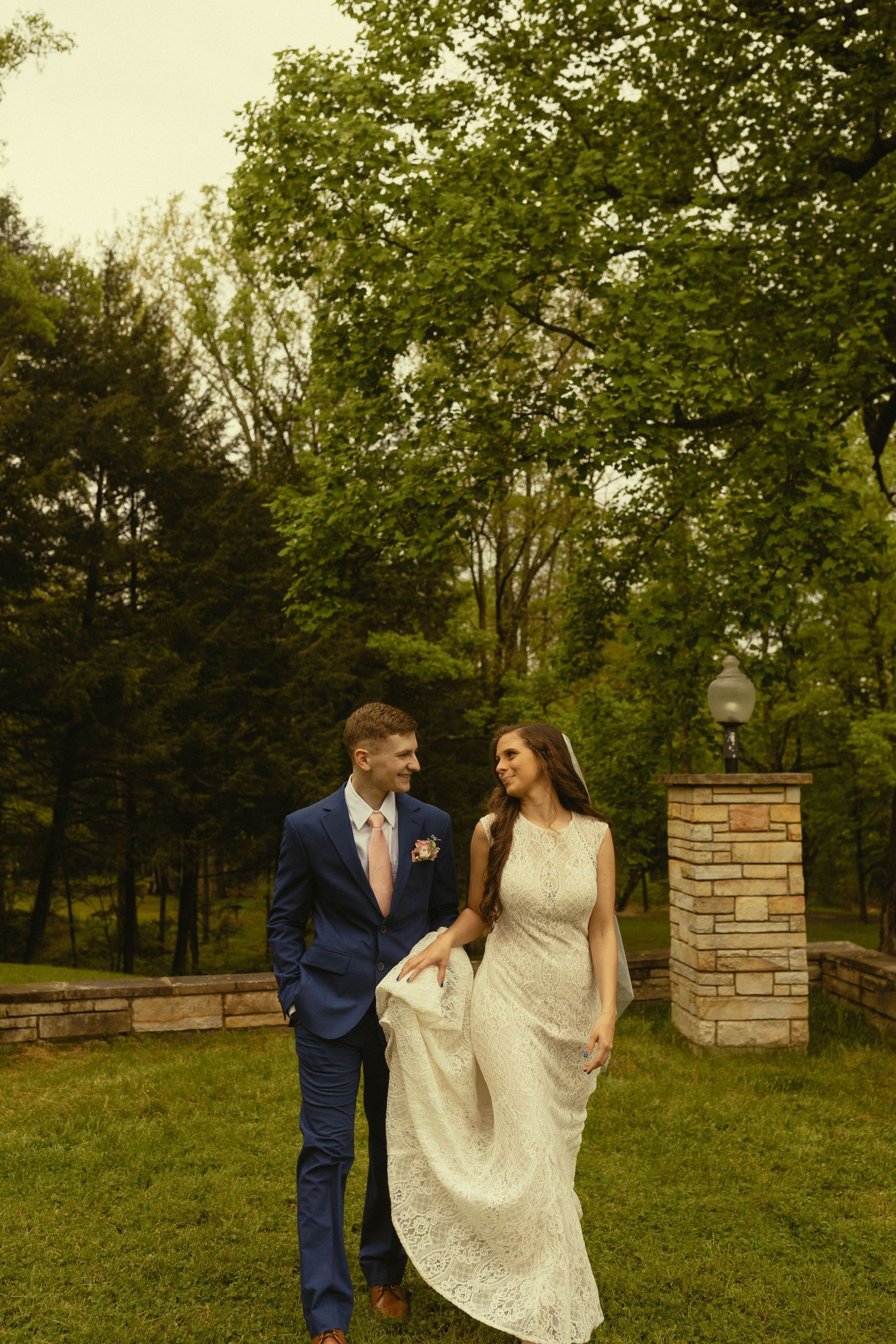A wedding couple shares a romantic moment on a grassy lawn with garden elements and trees in the background.