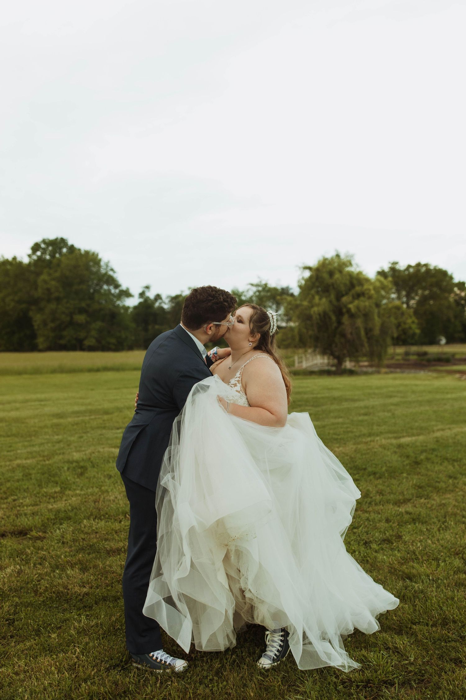 Couple shares romantic moment on grassy field with bride wearing flowing white gown.
