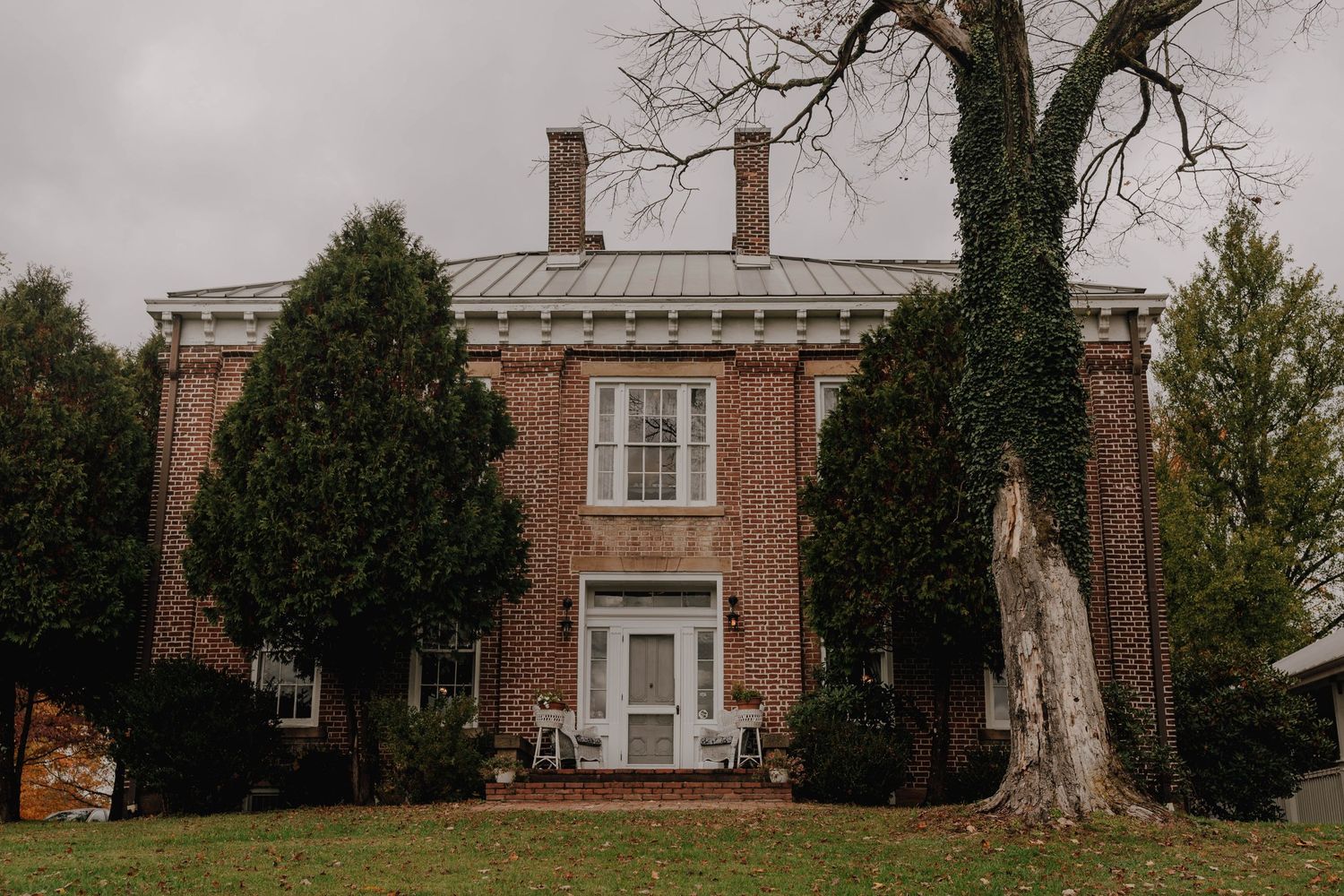A stately brick mansion with tall trees and white trim details.