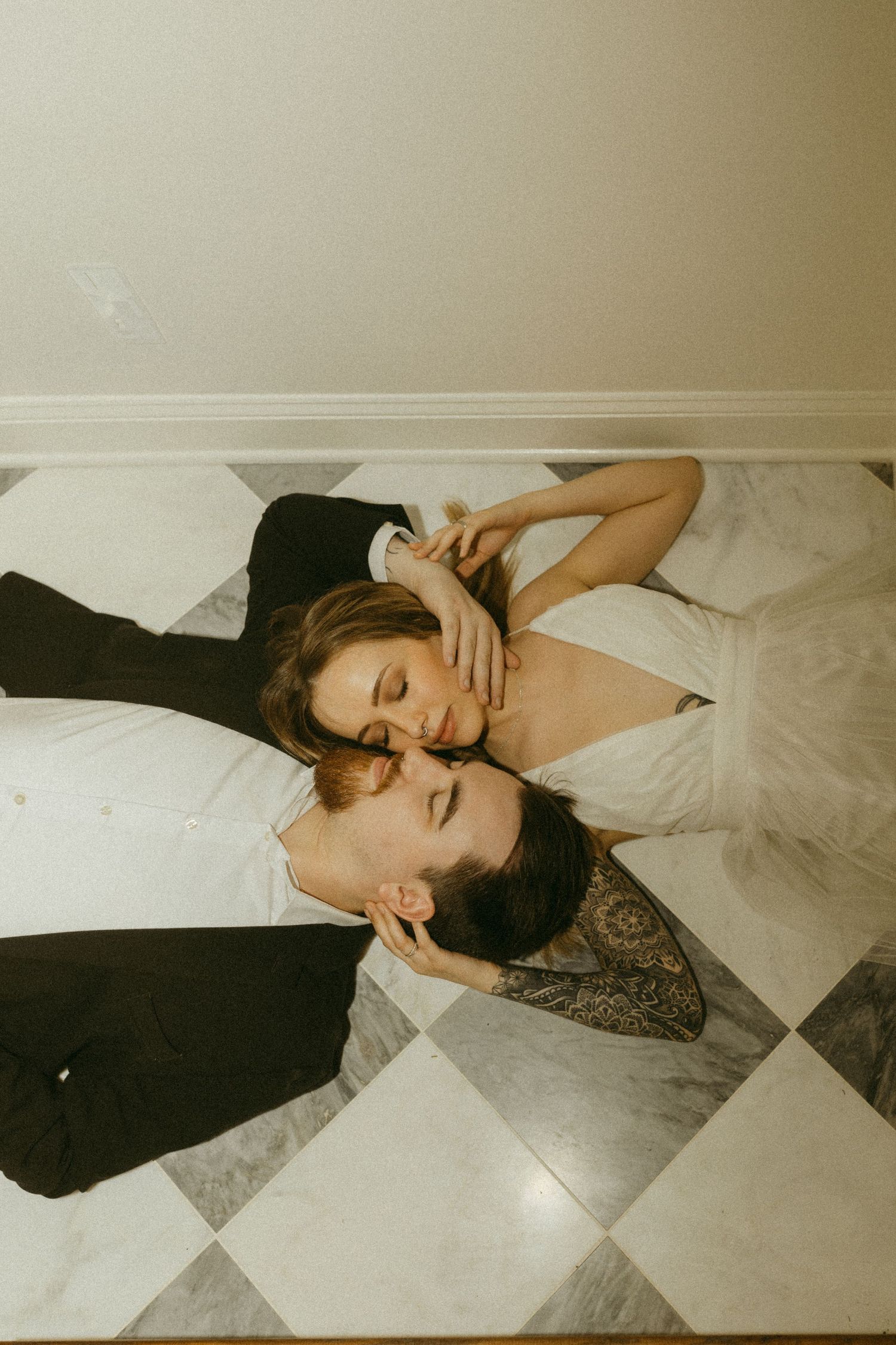 Overhead view of couple lying on checkered floor in formal attire.