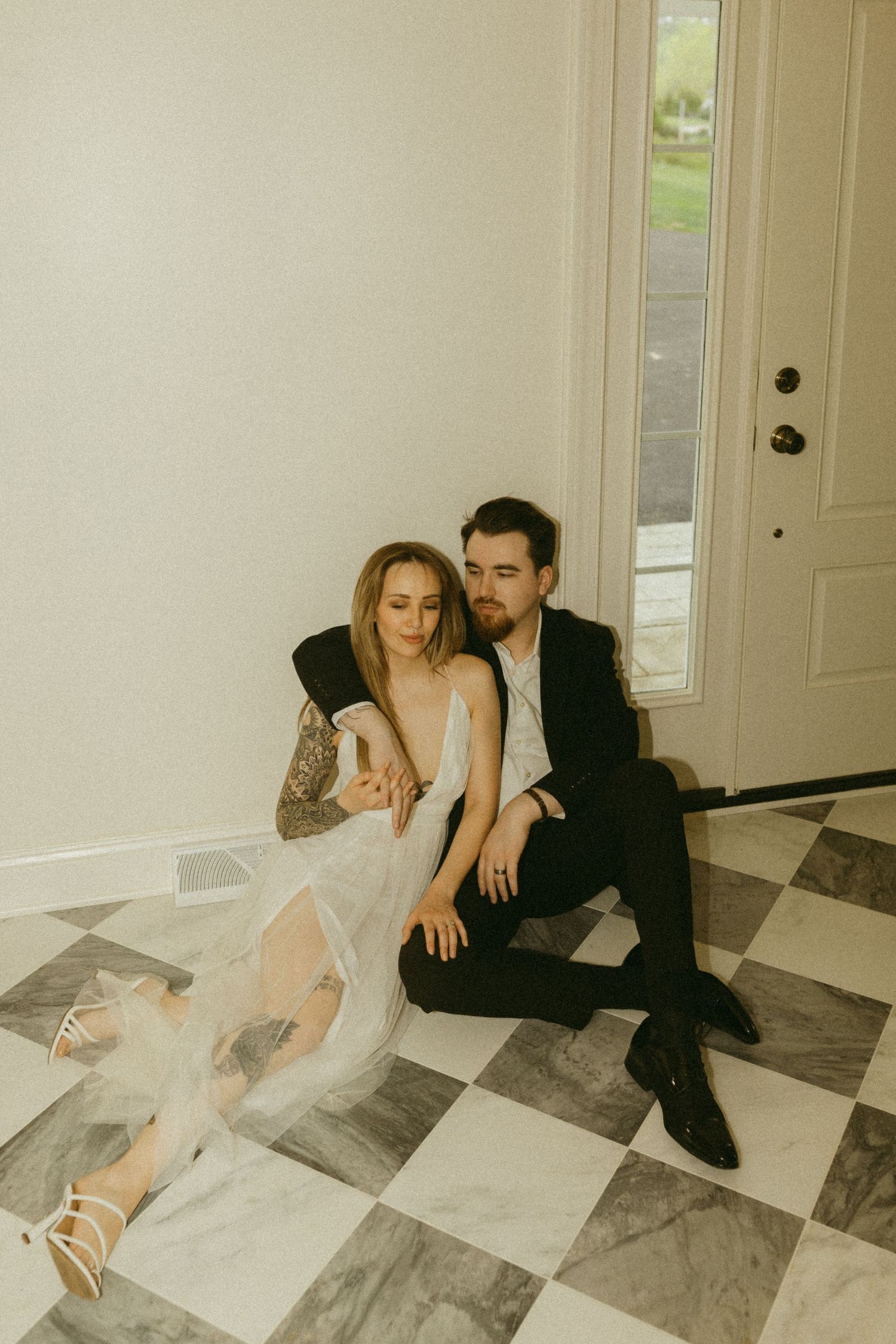 Moody portrait of couple in elegant attire on checkered marble flooring.