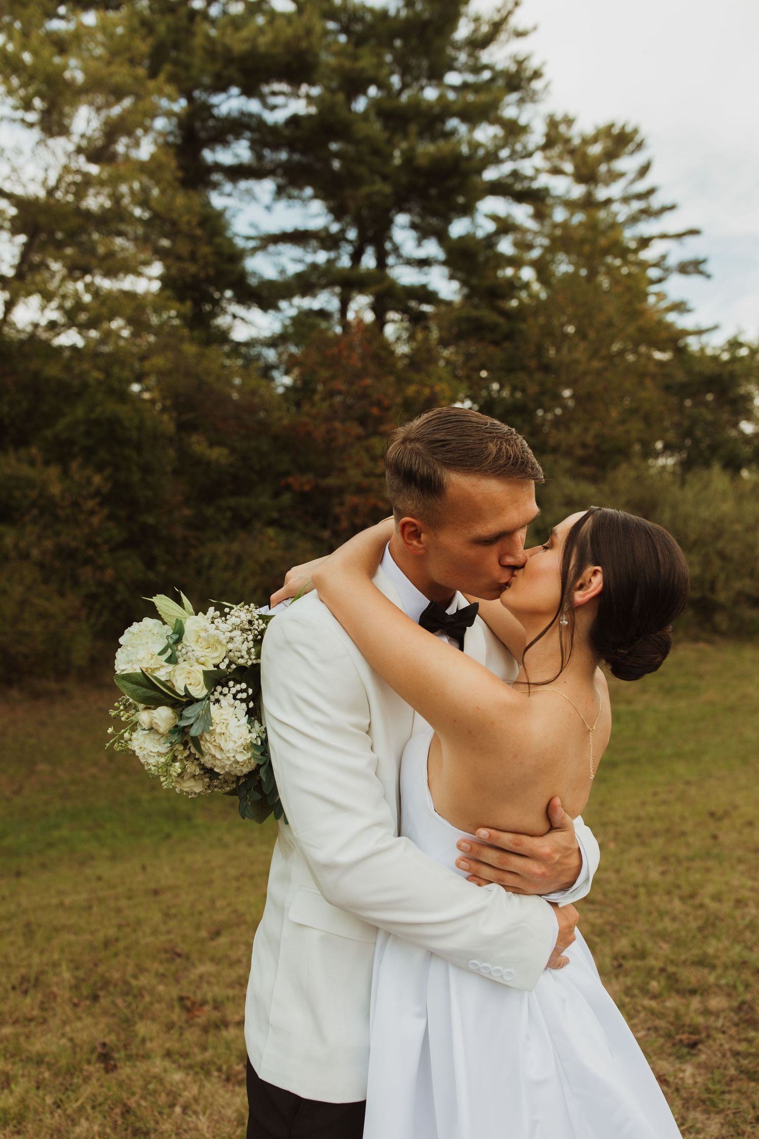 A romantic kiss between newlyweds with a white bouquet in a garden setting.
