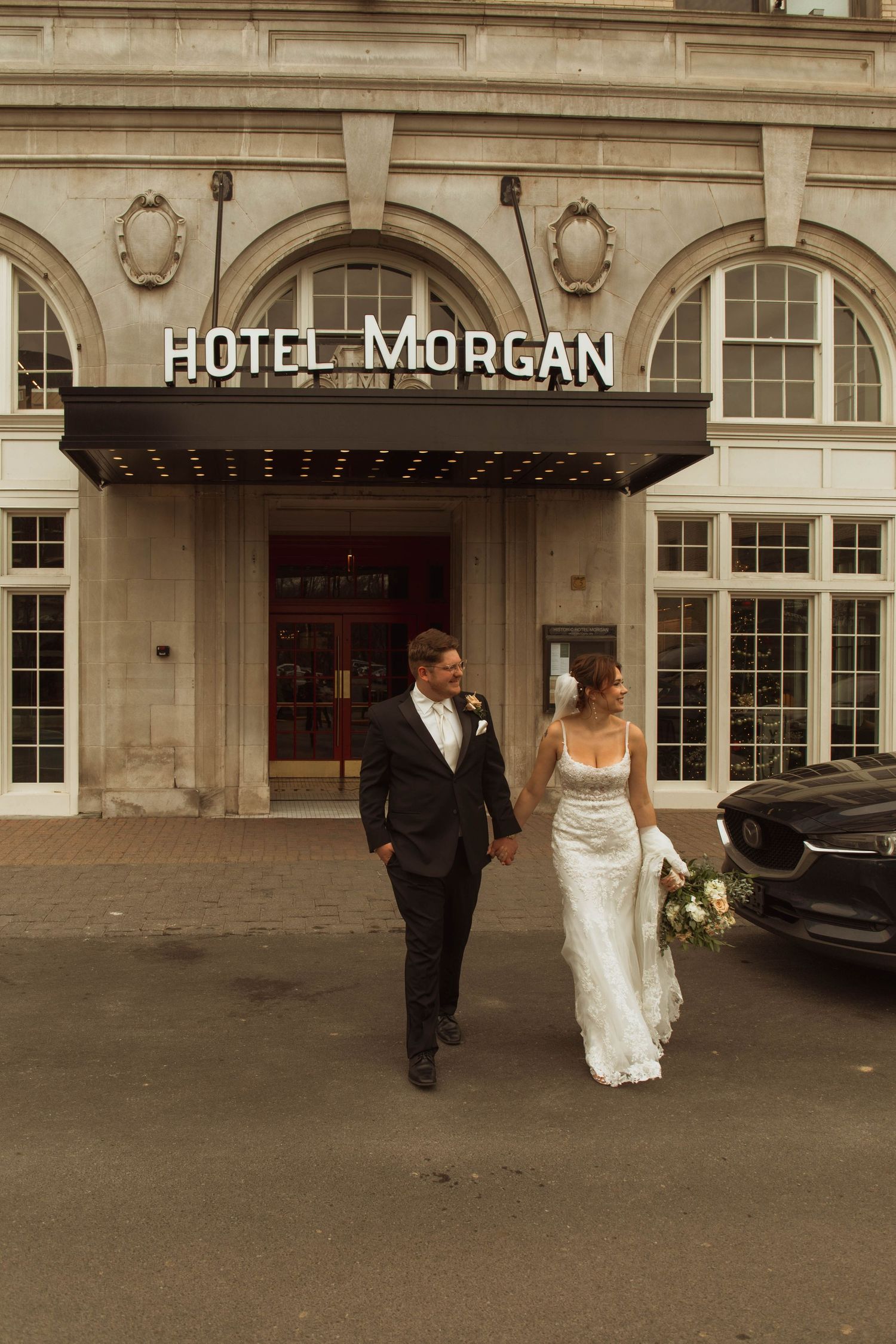 A wedding couple walks outside the classic Hotel Morgan building entrance in warm toned photography.