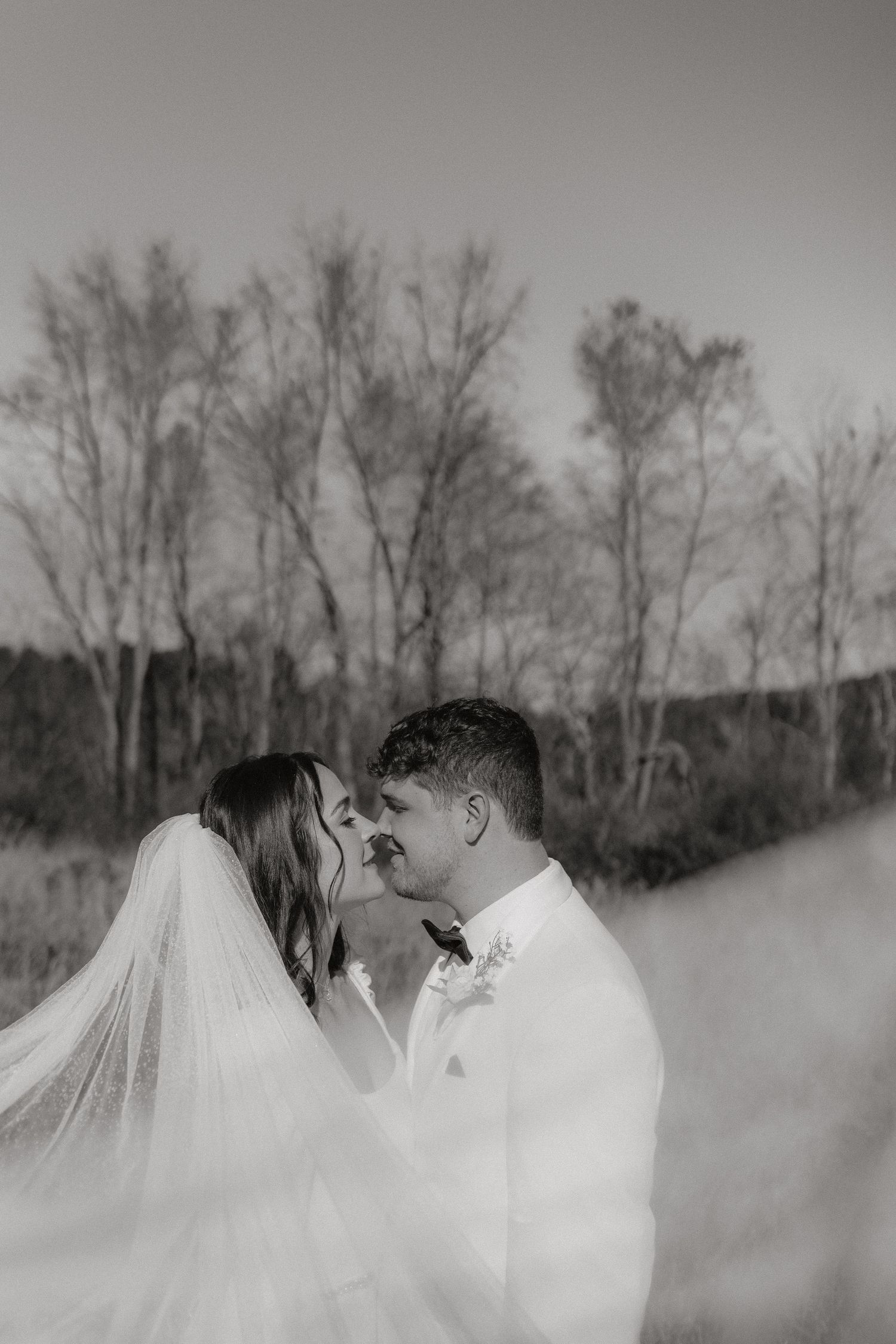 Ethereal black and white wedding portrait with veil flowing in winter landscape.