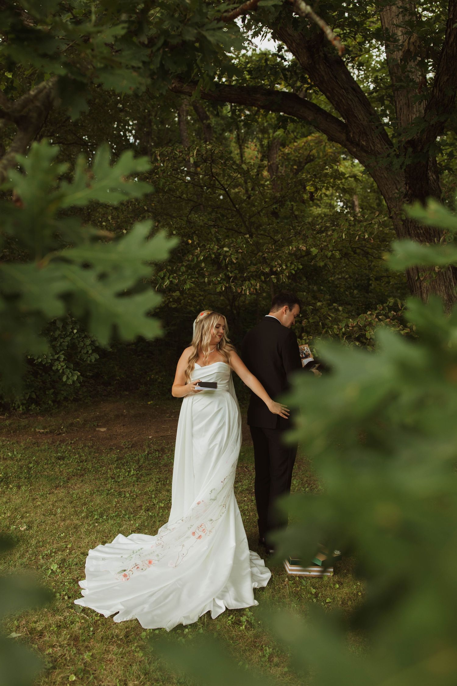 Couple in wedding attire sharing an intimate moment under a large tree in a garden setting.
