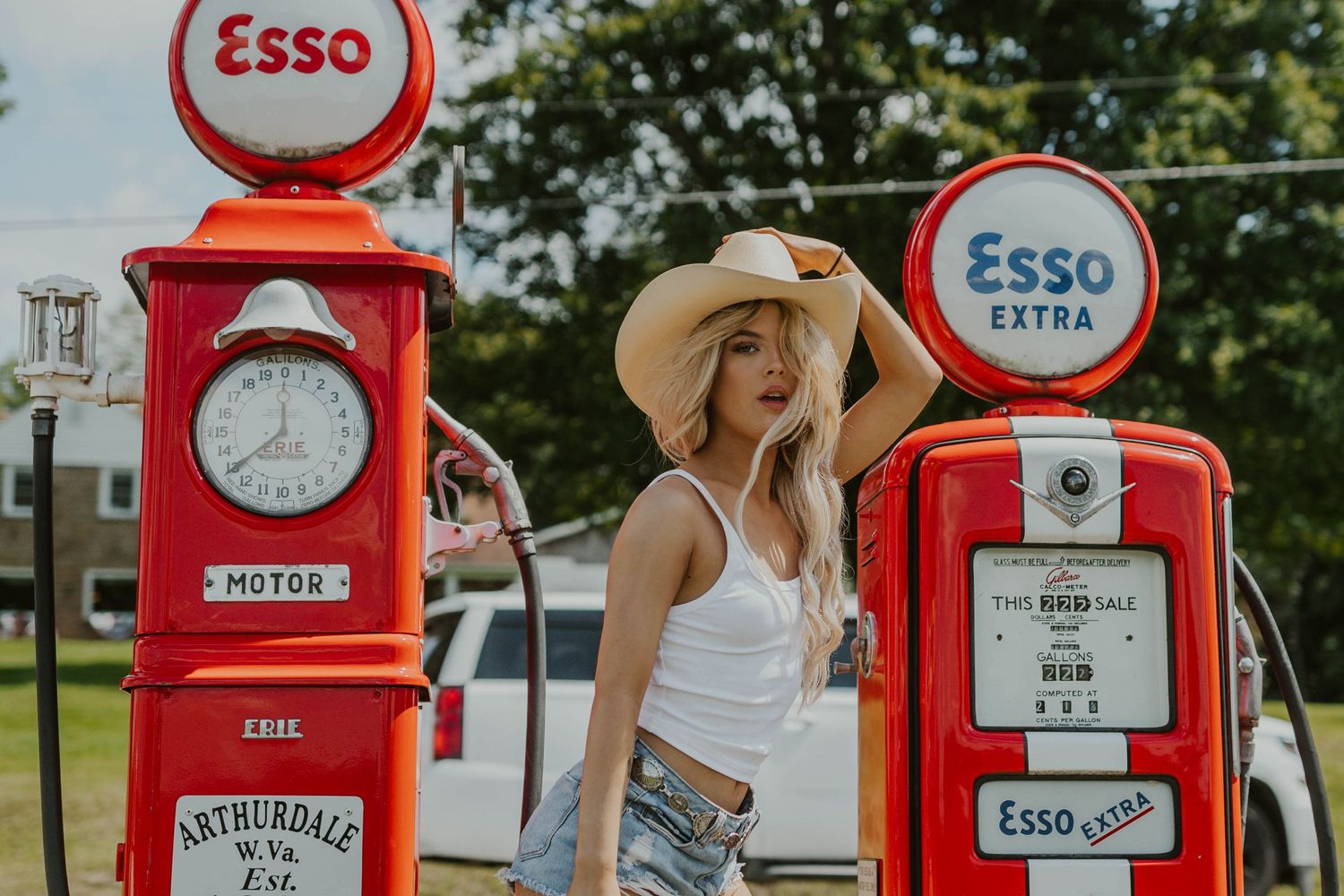 Two restored vintage Esso fuel pumps with round signs stand in bright sunlight.
