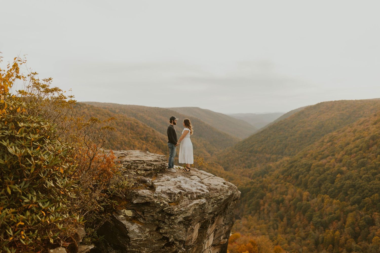 A couple stands on Hawks Nest overlook surrounded by fall foliage in the mountains at lindy point in blackwater falls state park