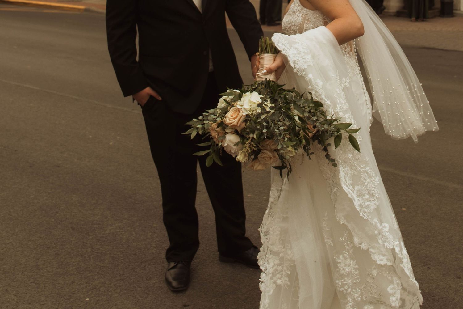 A close-up view of a wedding couple walking together with the bride holding an elegant white and green floral bouquet.