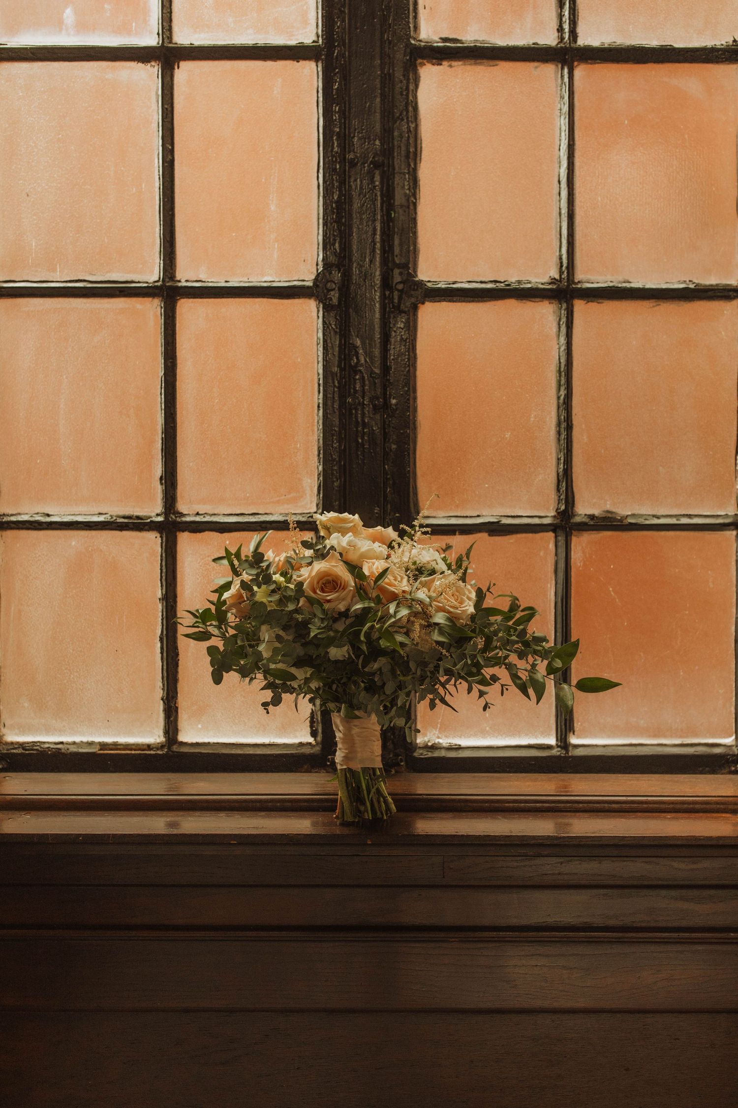 A vintage window frame showcases a delicate white and green wedding bouquet on the sill.
