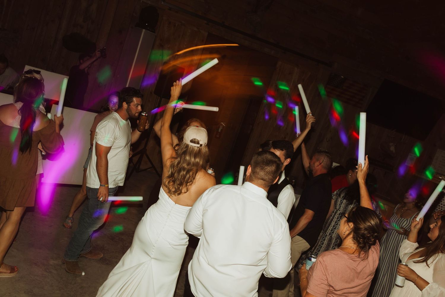 Wedding reception dance party with colorful lights and glow sticks on the dance floor.