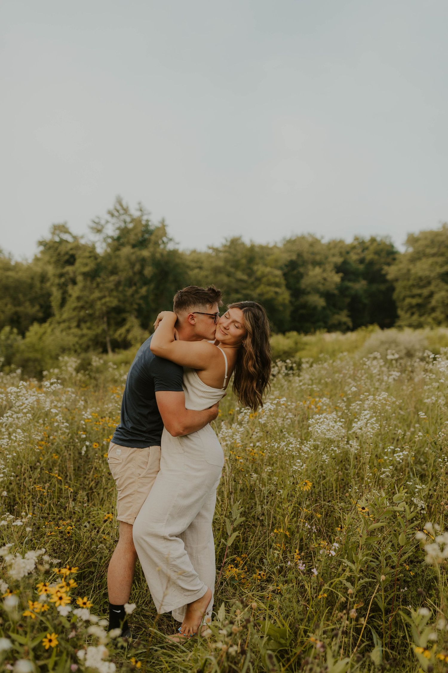 A tender moment between two people standing in a summer meadow filled with wildflowers.