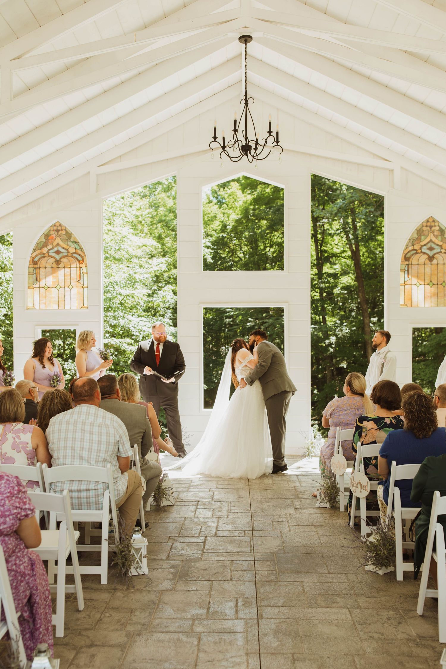 Beautiful indoor chapel wedding ceremony with guests seated in white chairs under a vaulted ceiling.