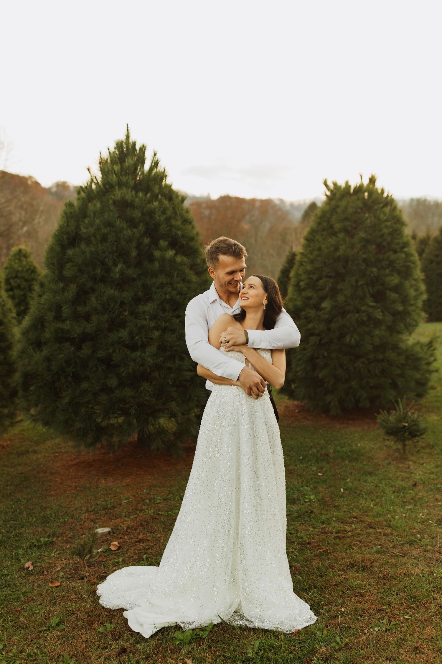 Intimate wedding portrait at a Christmas tree farm during sunset with warm golden light.