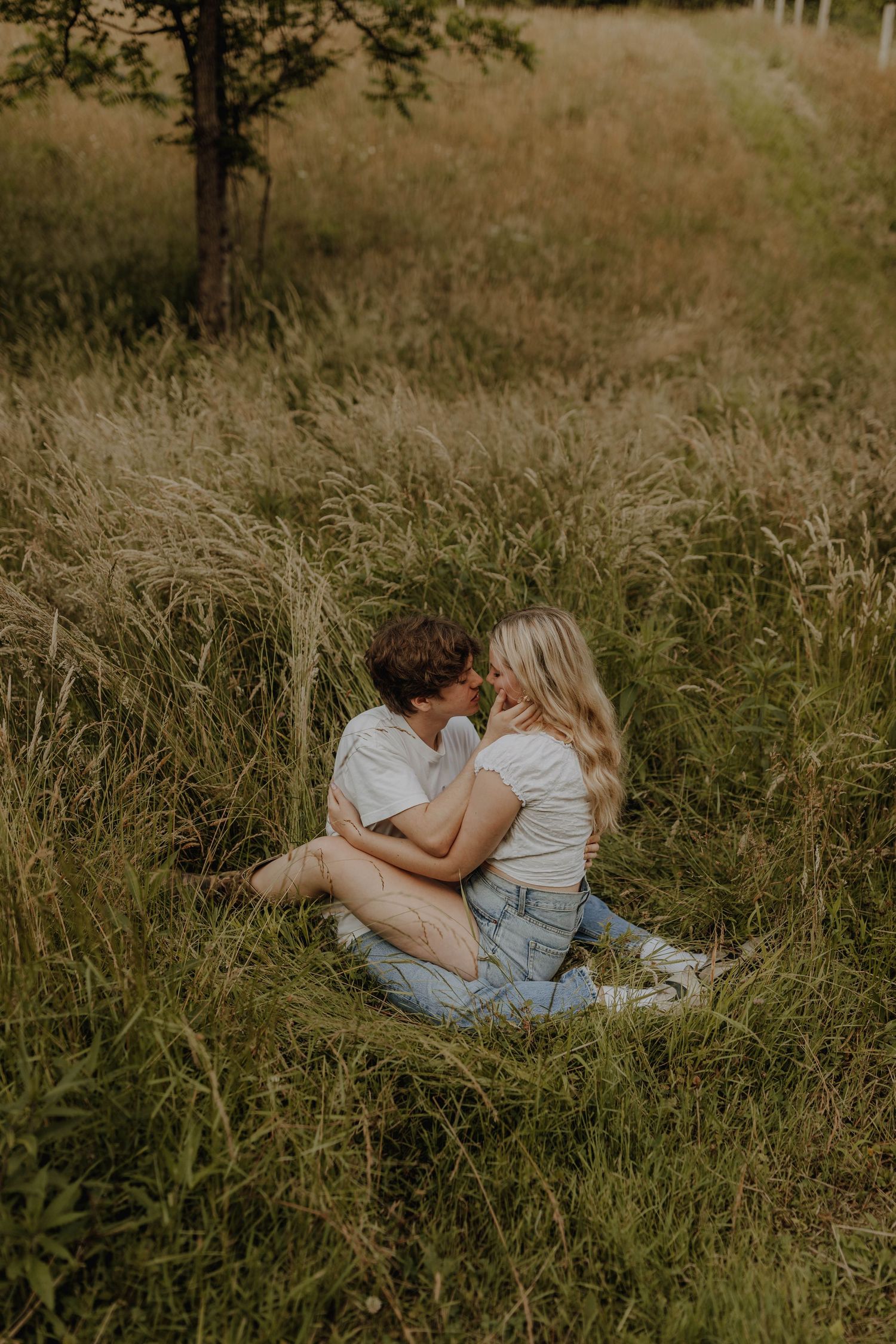 A romantic moment shared between two people sitting in tall golden grass during sunset.