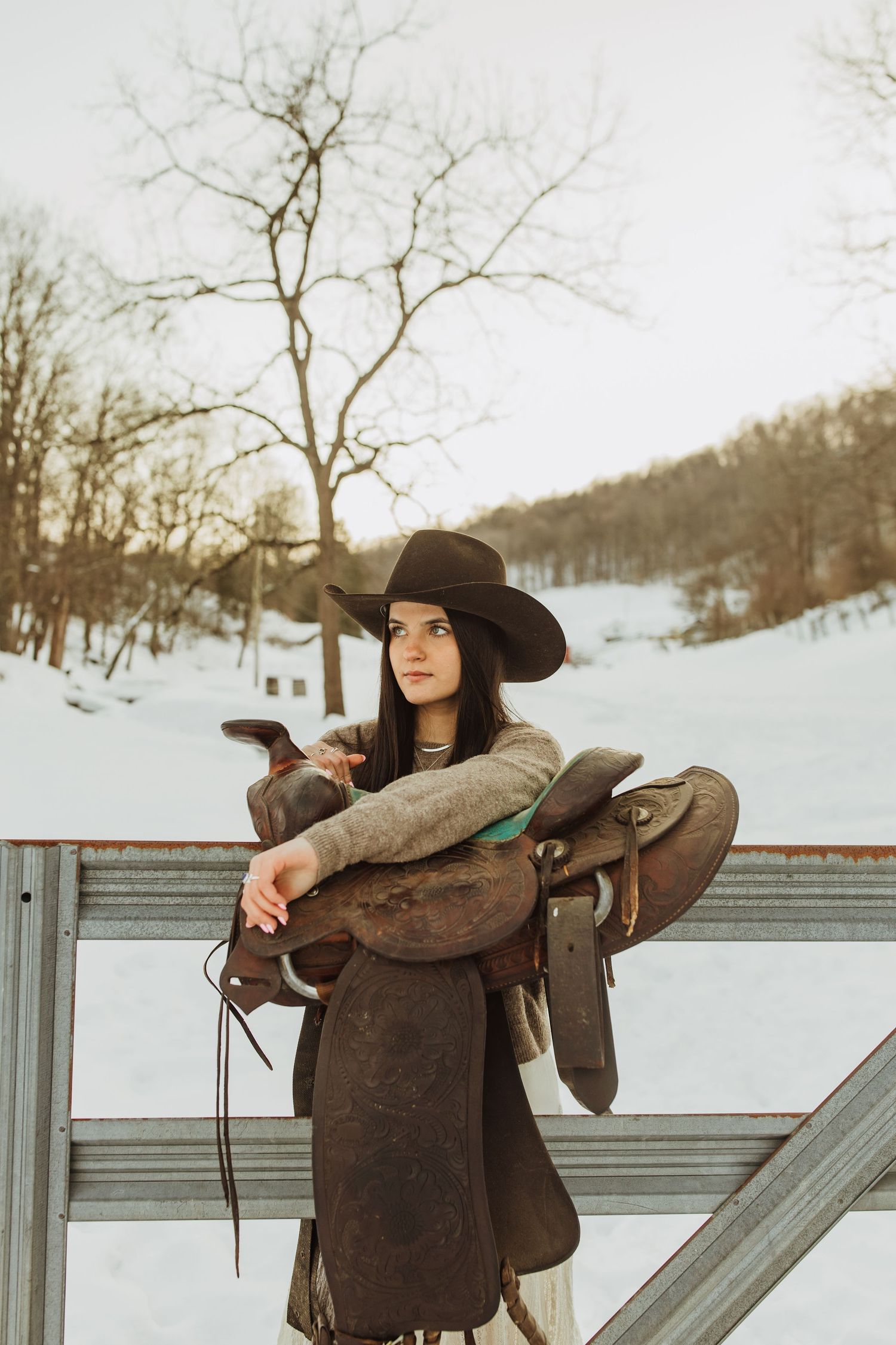 A rustic western portrait with leather saddle and hat against snowy backdrop.