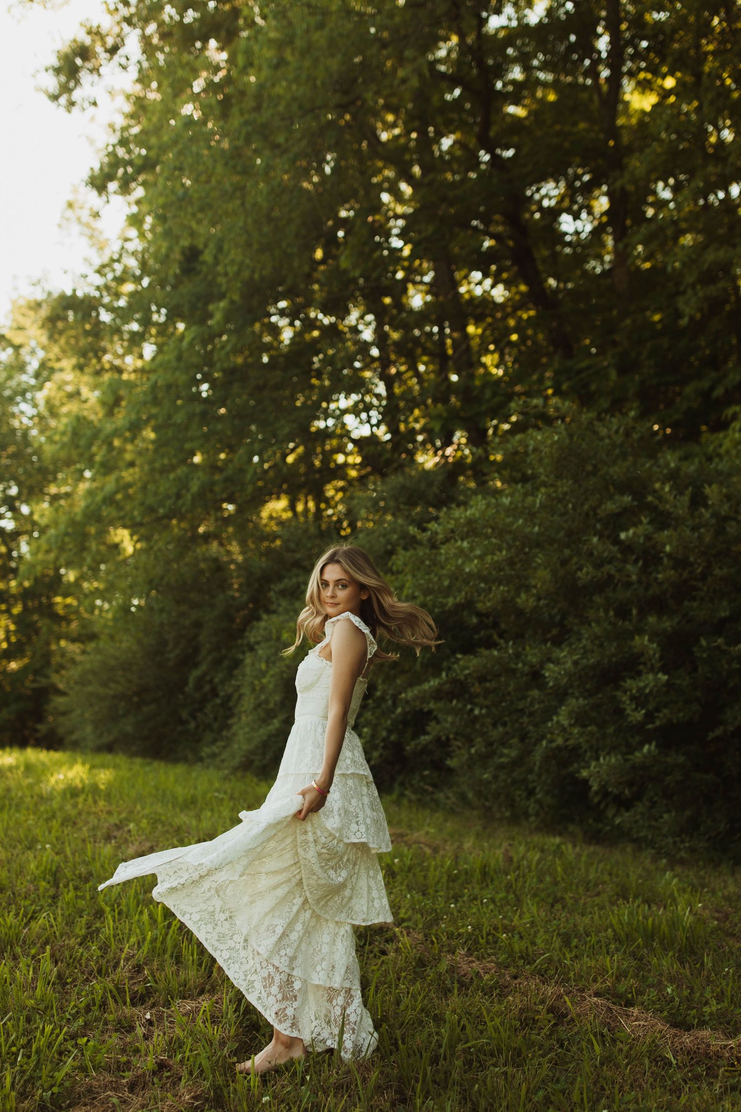 A flowing white dress twirls gracefully in motion against a sunlit forest background.