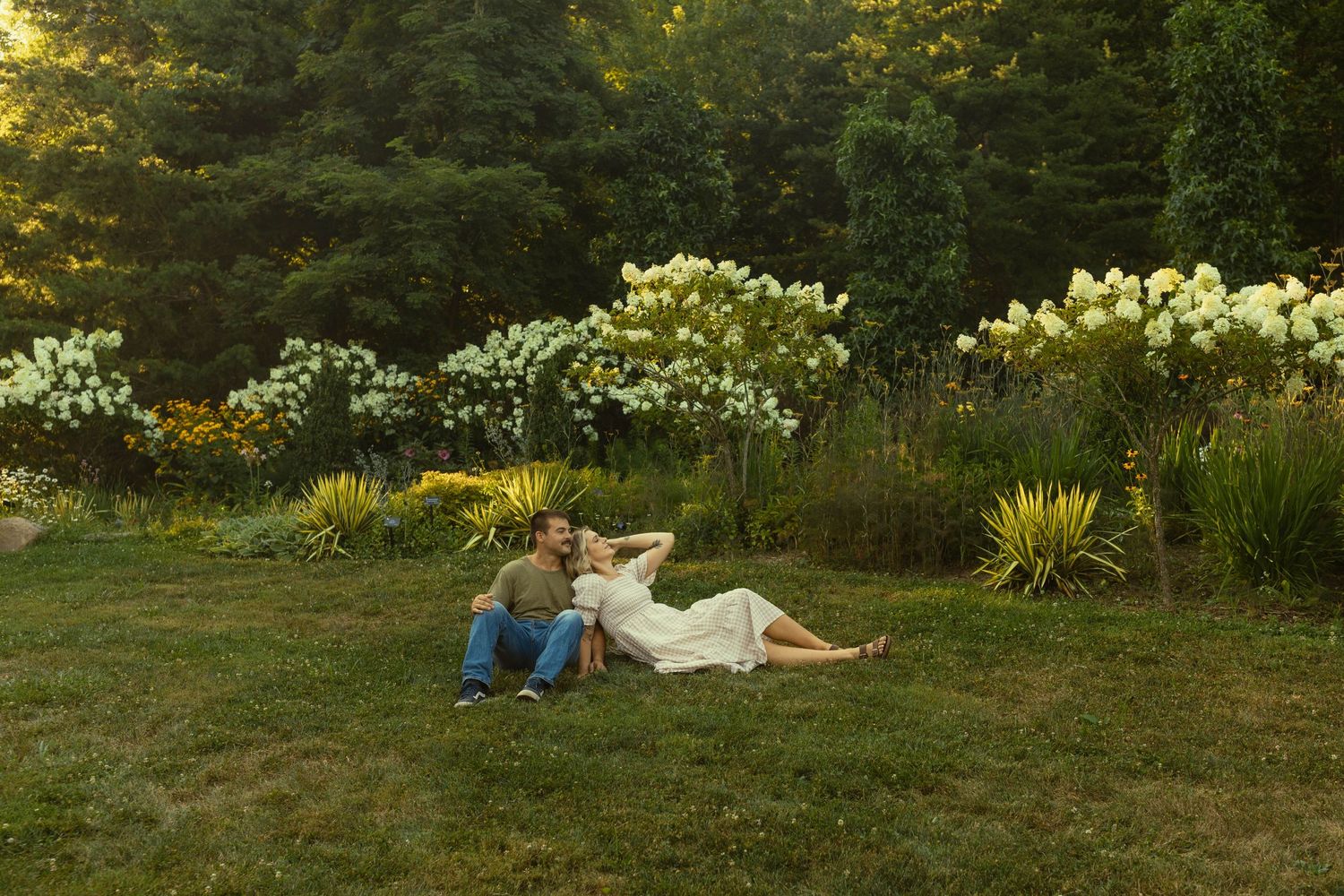 A couple relaxes o in a lush garden setting during golden hour as sunlight filters through trees at the west virginia botanical gardens.