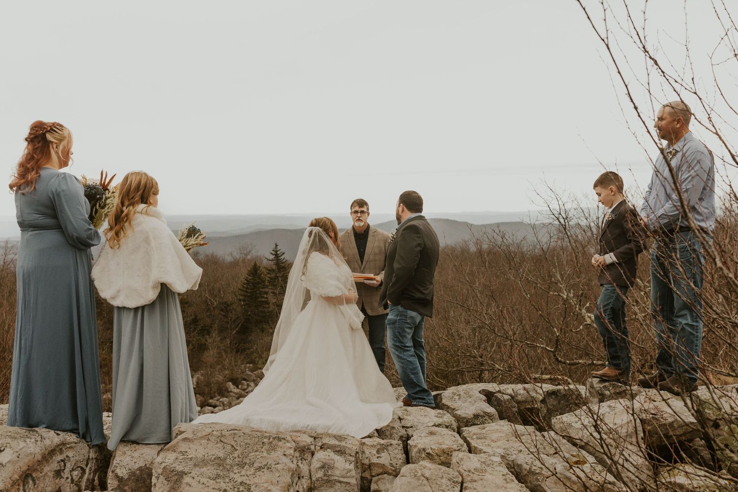 Wedding ceremony taking place on rocky outcrop with guests watching.