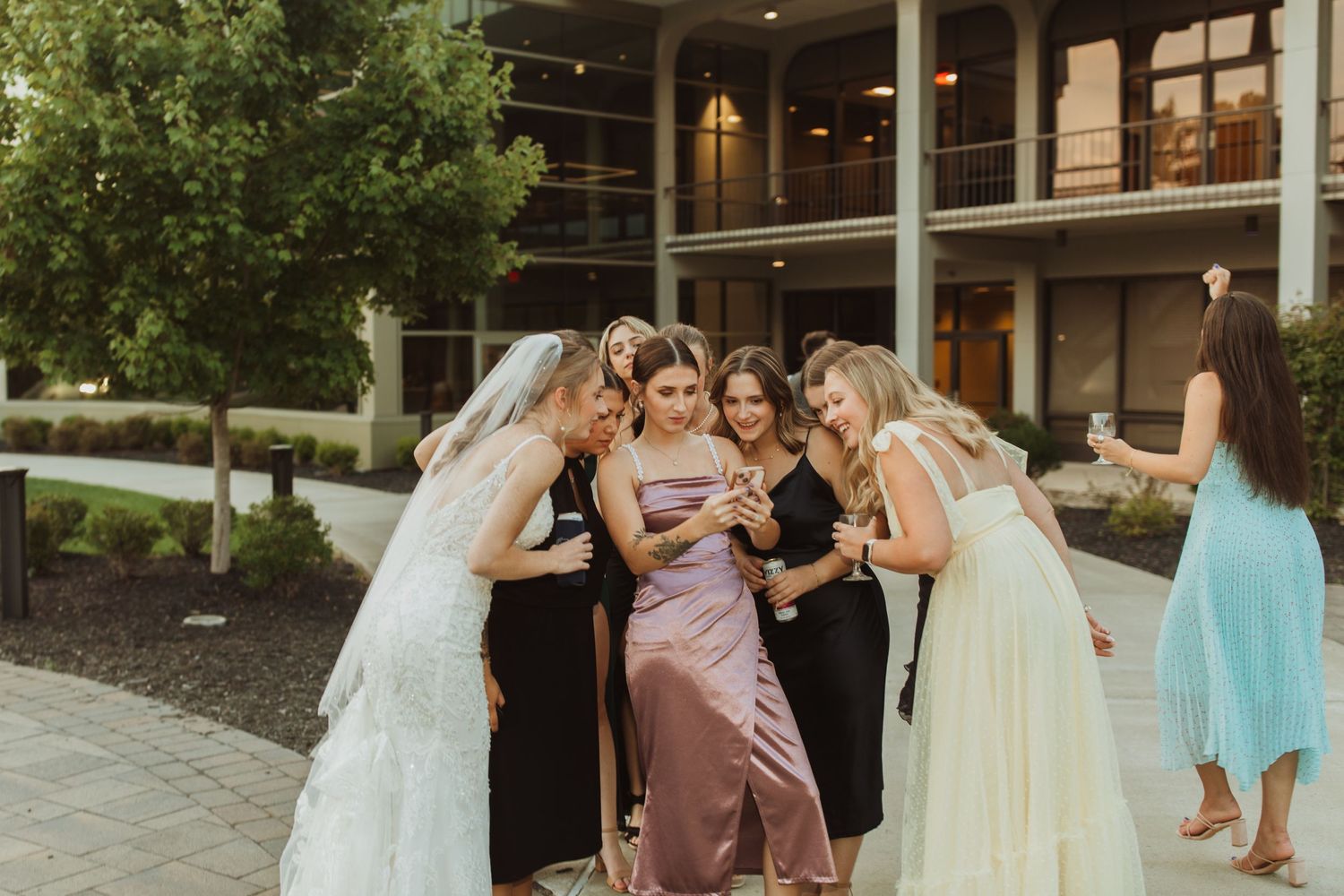 Group of wedding attendees in formal attire share laughter and poses together outdoors.