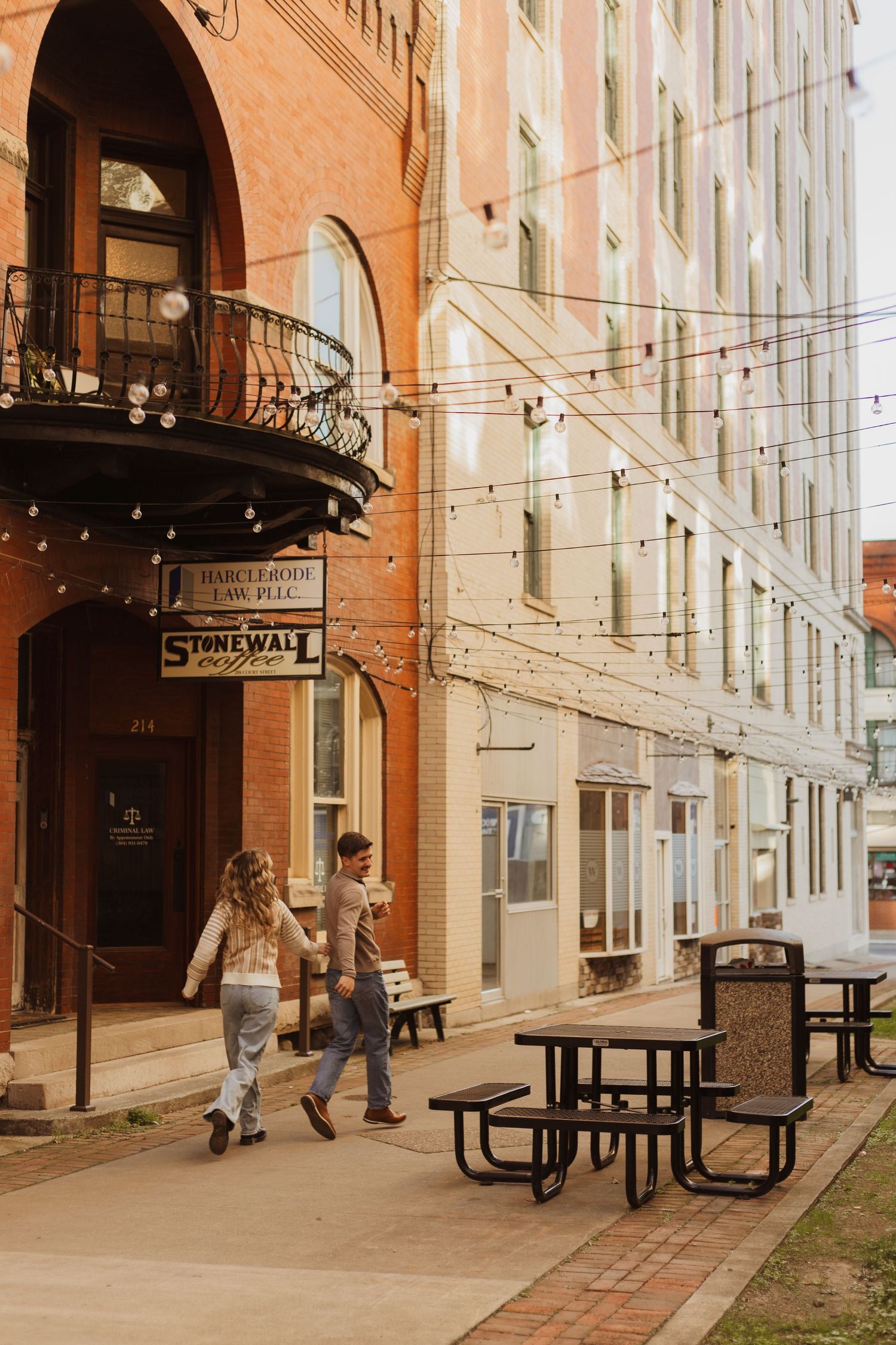 Two people walking hand in hand beneath string lights outside the Stonewall Cafe building.