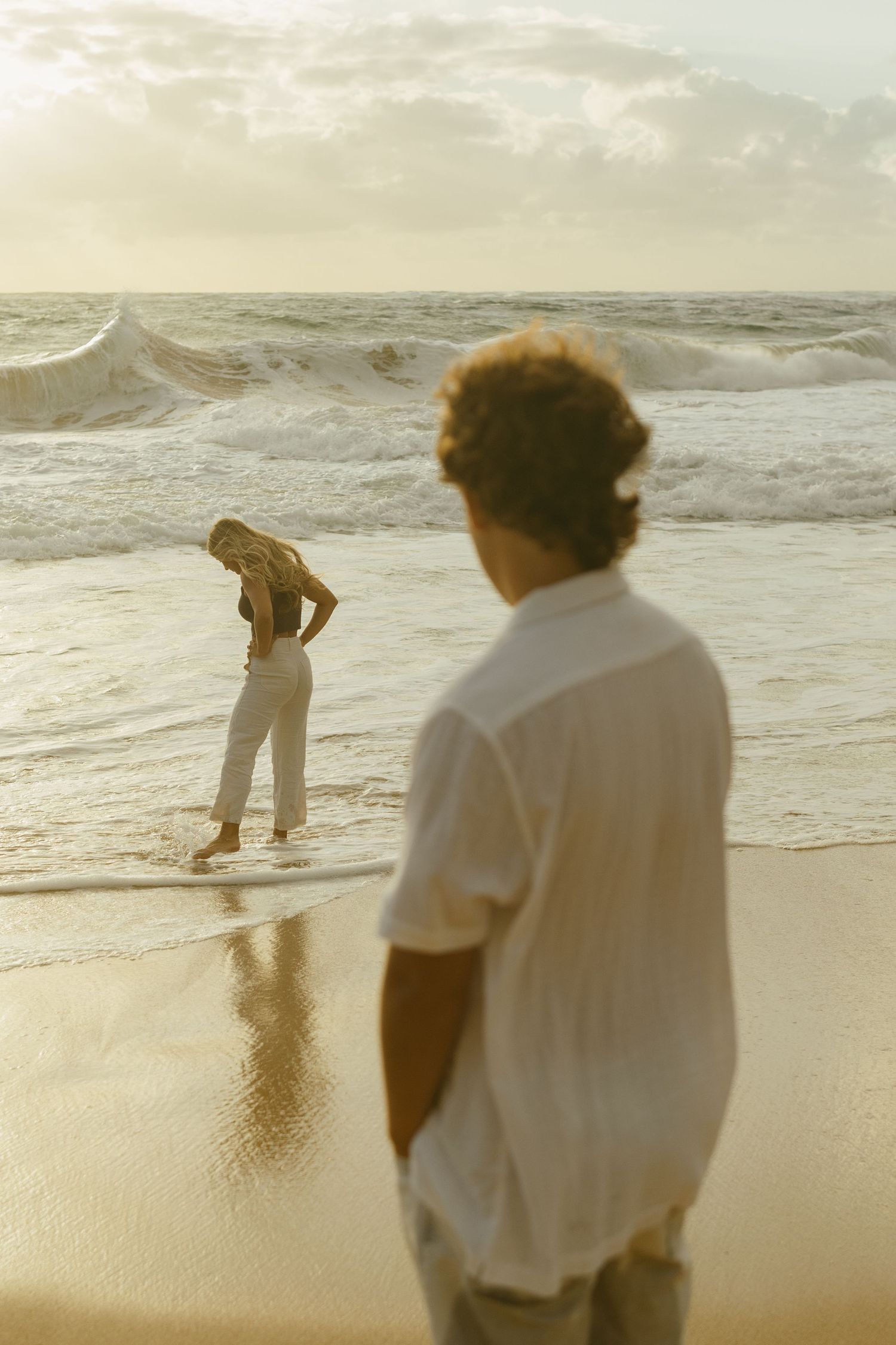 Two people sharing a sunset moment on a golden beach with crashing waves.