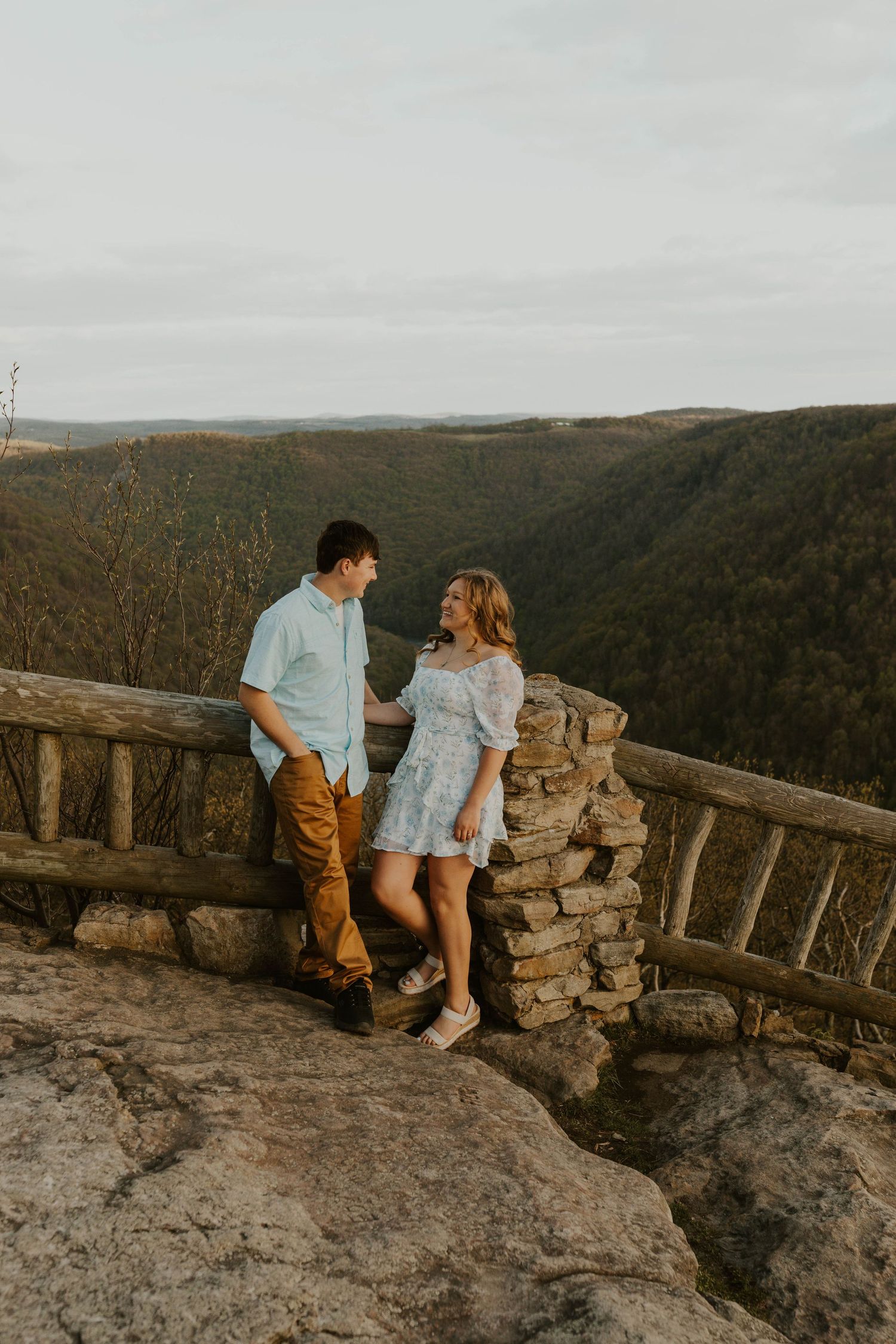 A couple shares a romantic moment at a scenic mountain overlook with stone railing at sunset at coopers rock