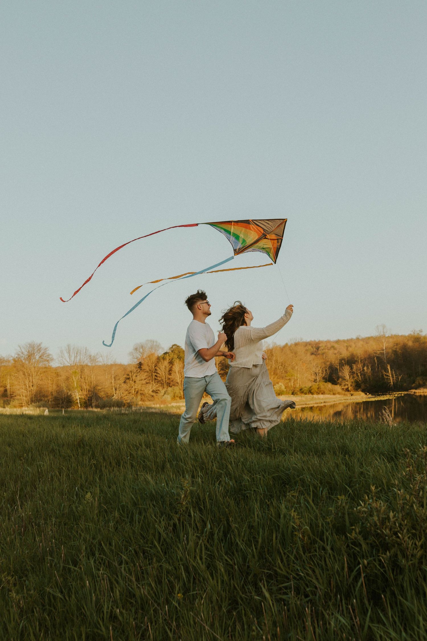 A pair flies a colorful kite together in a sunlit meadow during golden hour.