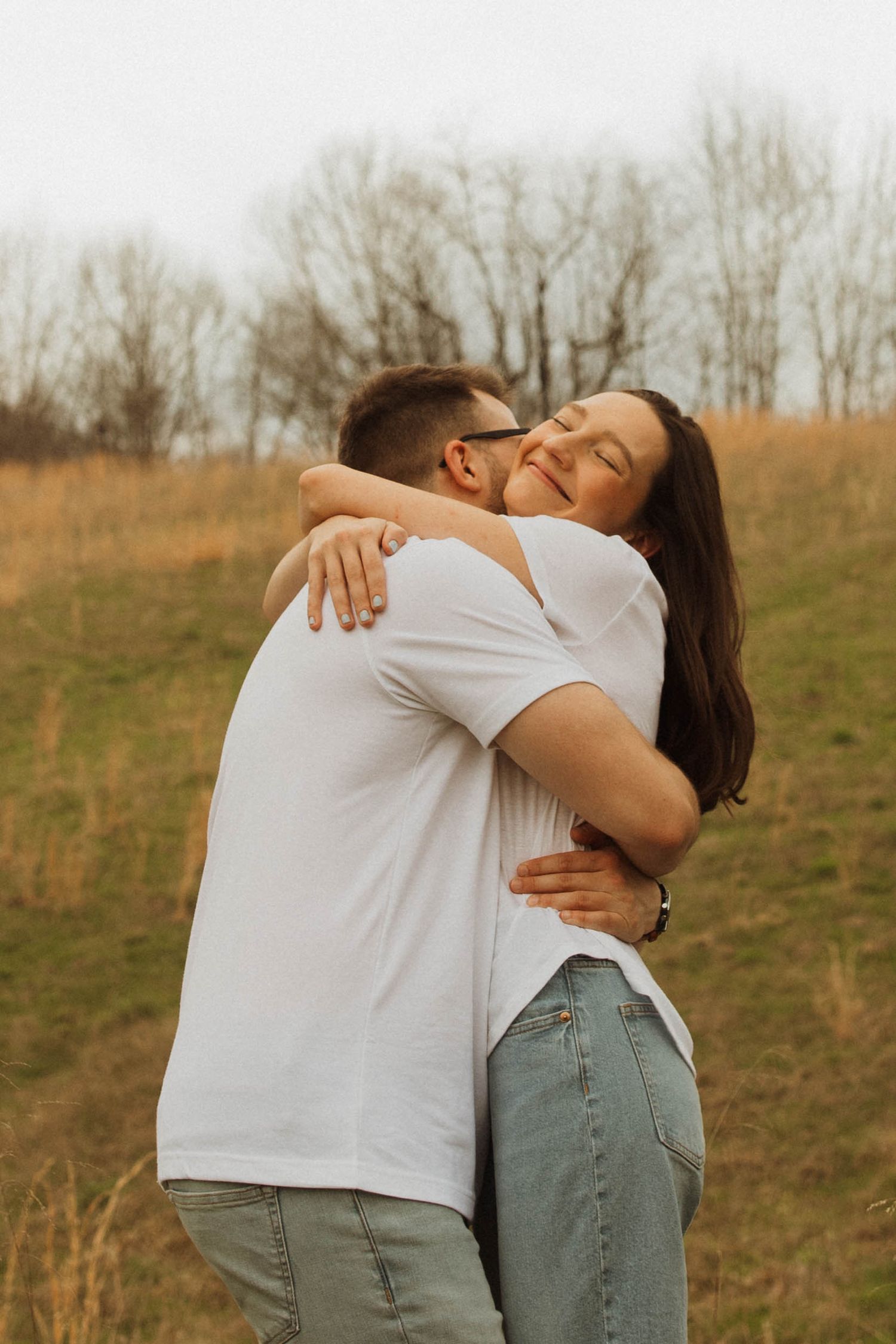 Couple embracing in warm afternoon light on grassy hillside.