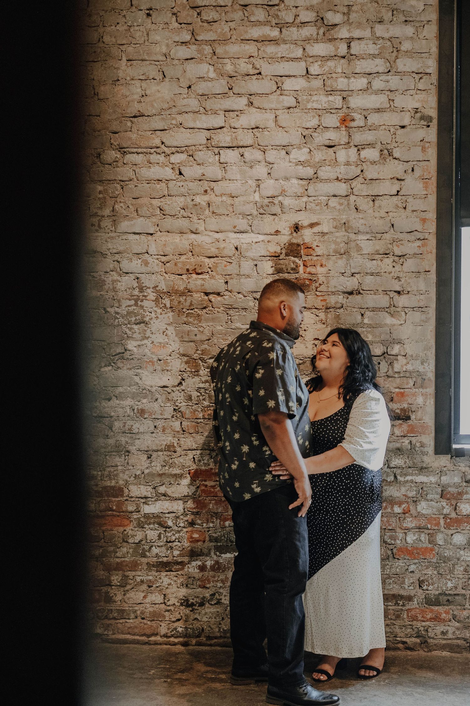 Couple sharing an intimate moment against rustic brick wall.