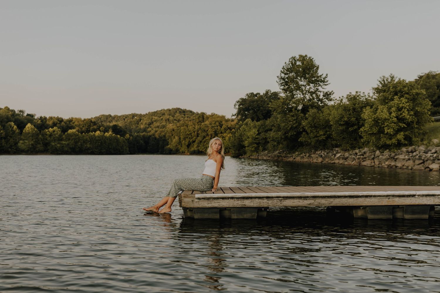 Person splashing into calm lake water from wooden dock during sunset.